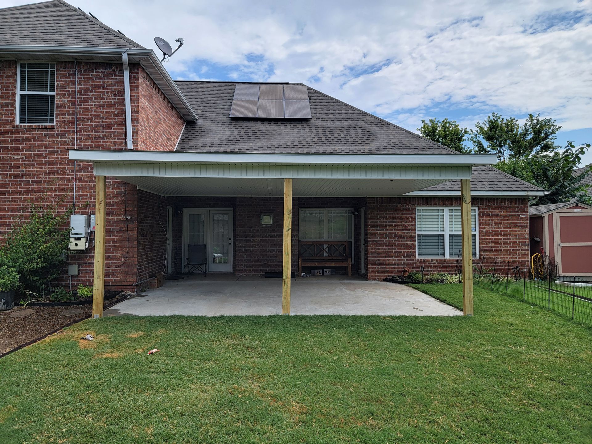 Brick house patio with covered concrete slab, lawn, and solar panels on the roof