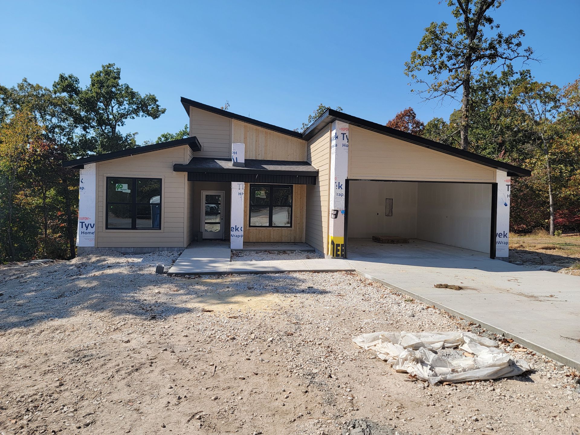 Partially built suburban house with unfinished driveway and dirt front yard under a clear blue sky