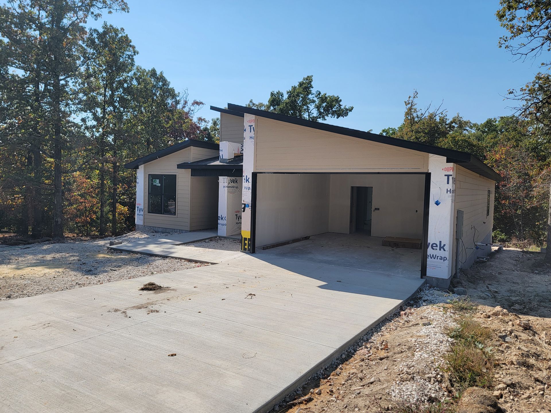 Single-story beige house under construction with a large garage opening and concrete driveway