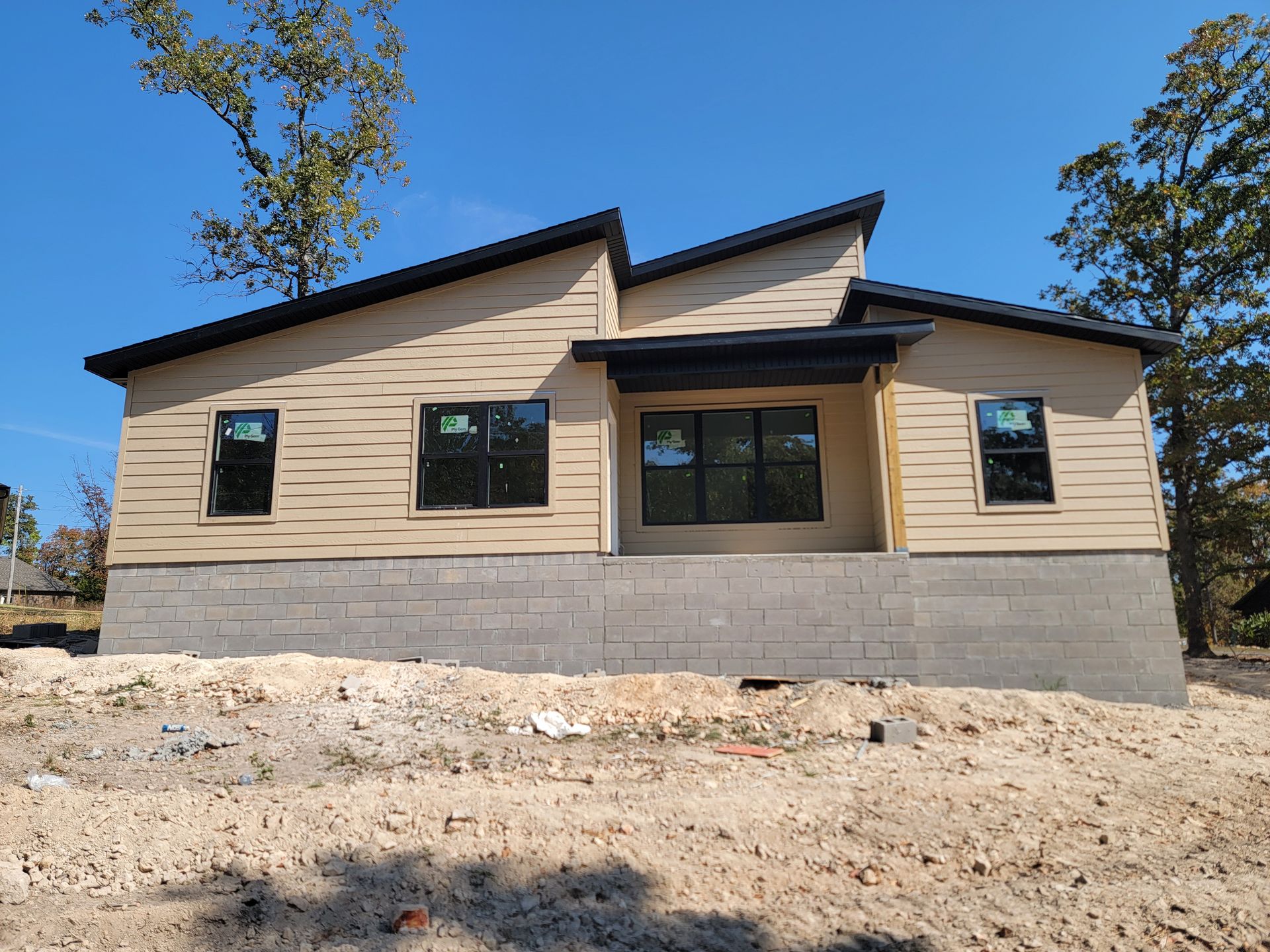 New beige house with black-trimmed windows and stone foundation on a dirt lot