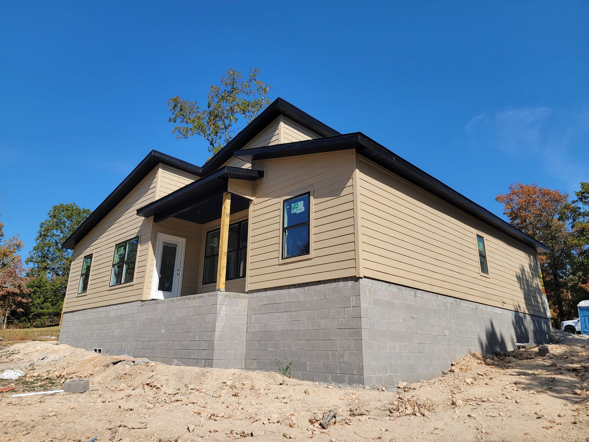 New house with beige siding and gray foundation under construction on a clear blue sky day