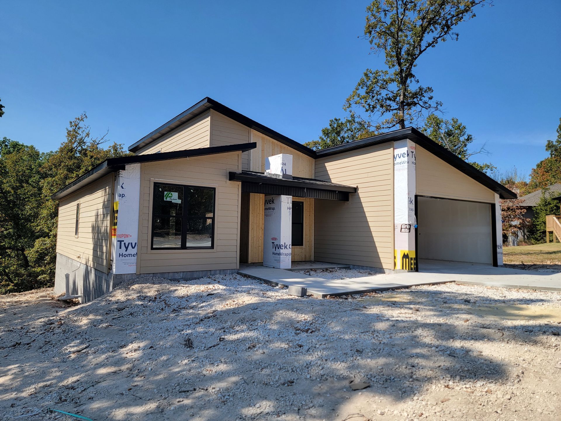 Front view of a small beige house under construction with a gravel driveway and garage.