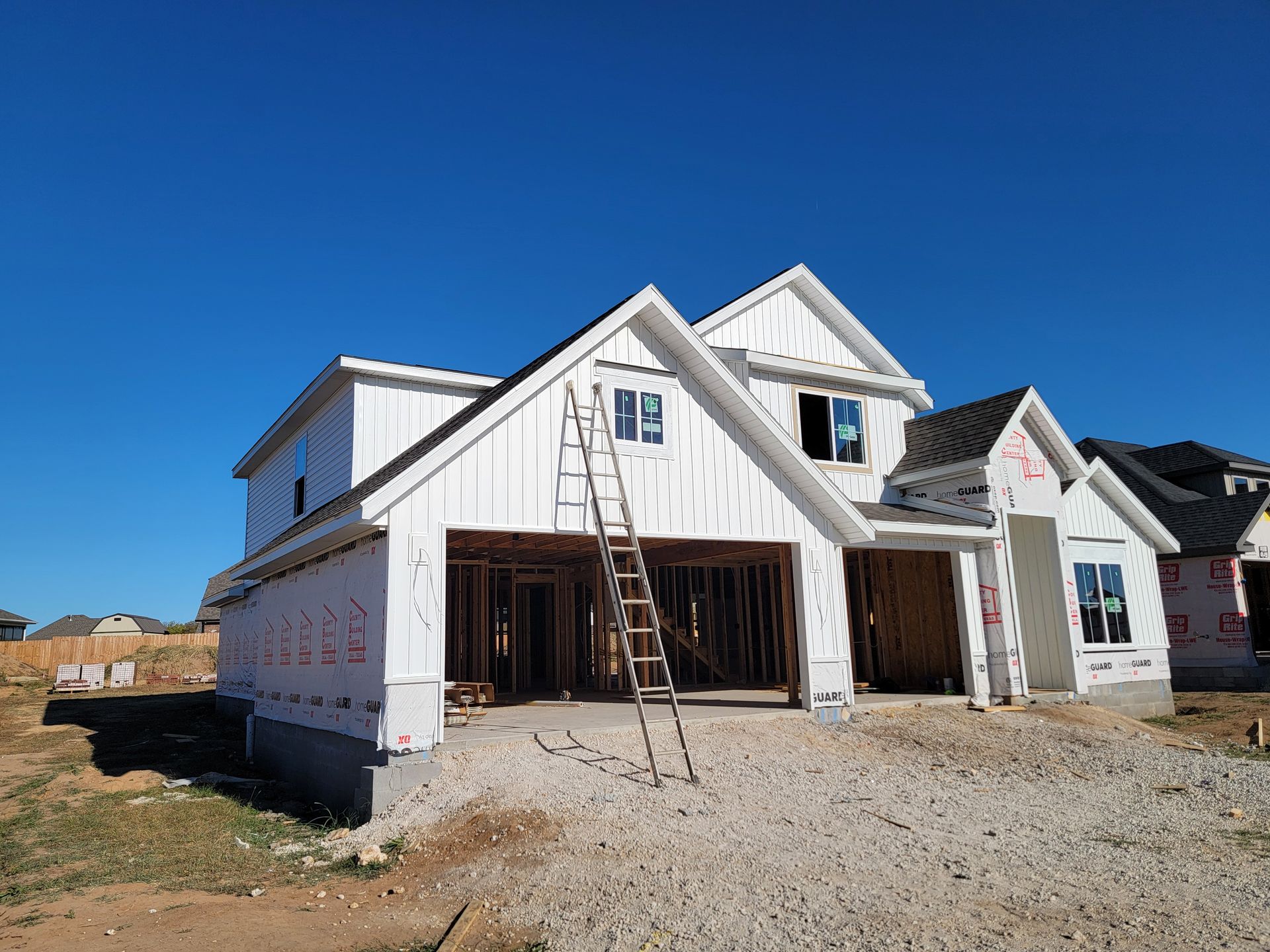 New white house under construction with open garage and ladders on a gravel lot