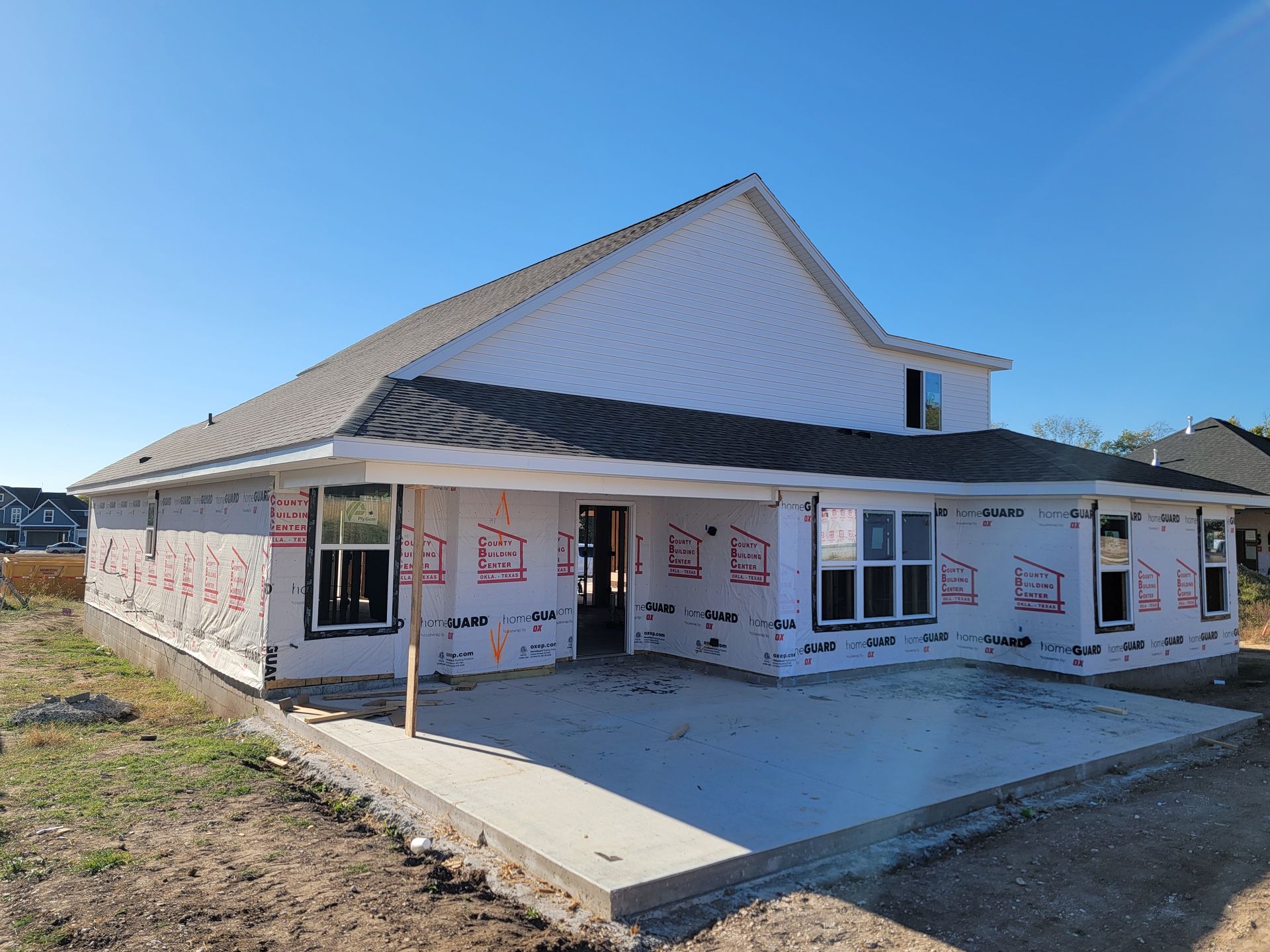 Partially built house with white siding, gray roof, and front concrete porch under a clear blue sky
