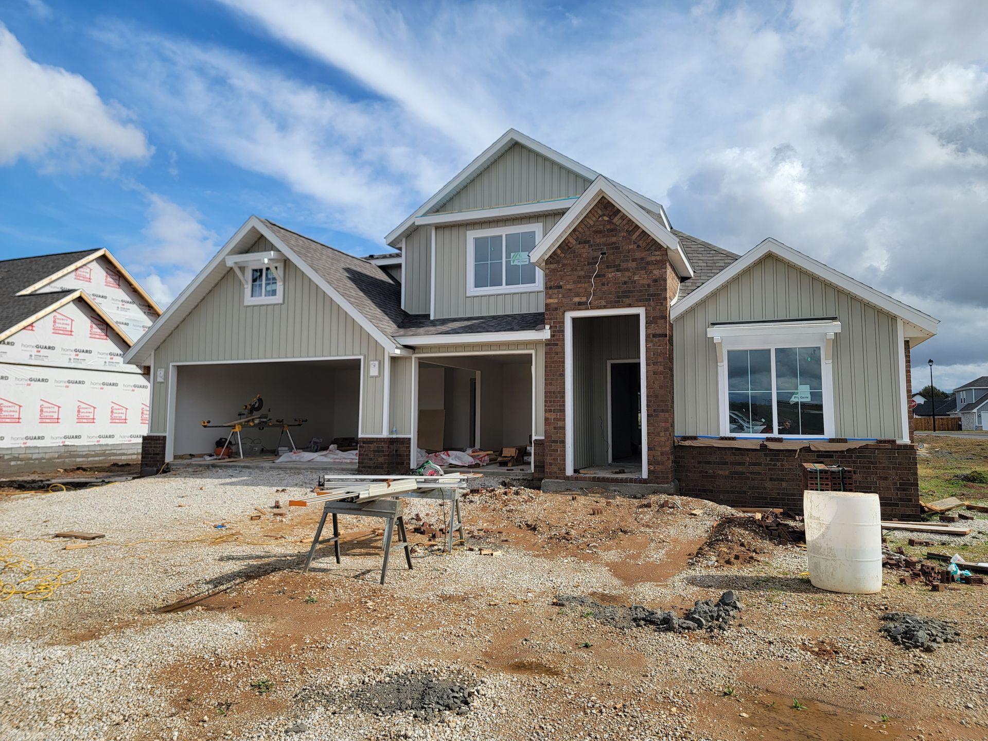 New house under construction with unfinished siding, brick facade, and a gravel front yard under blue sky
