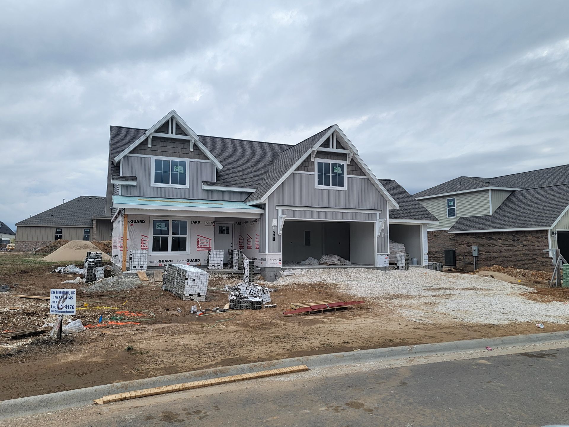 New house under construction with gray siding, unfinished driveway, and muddy front yard.