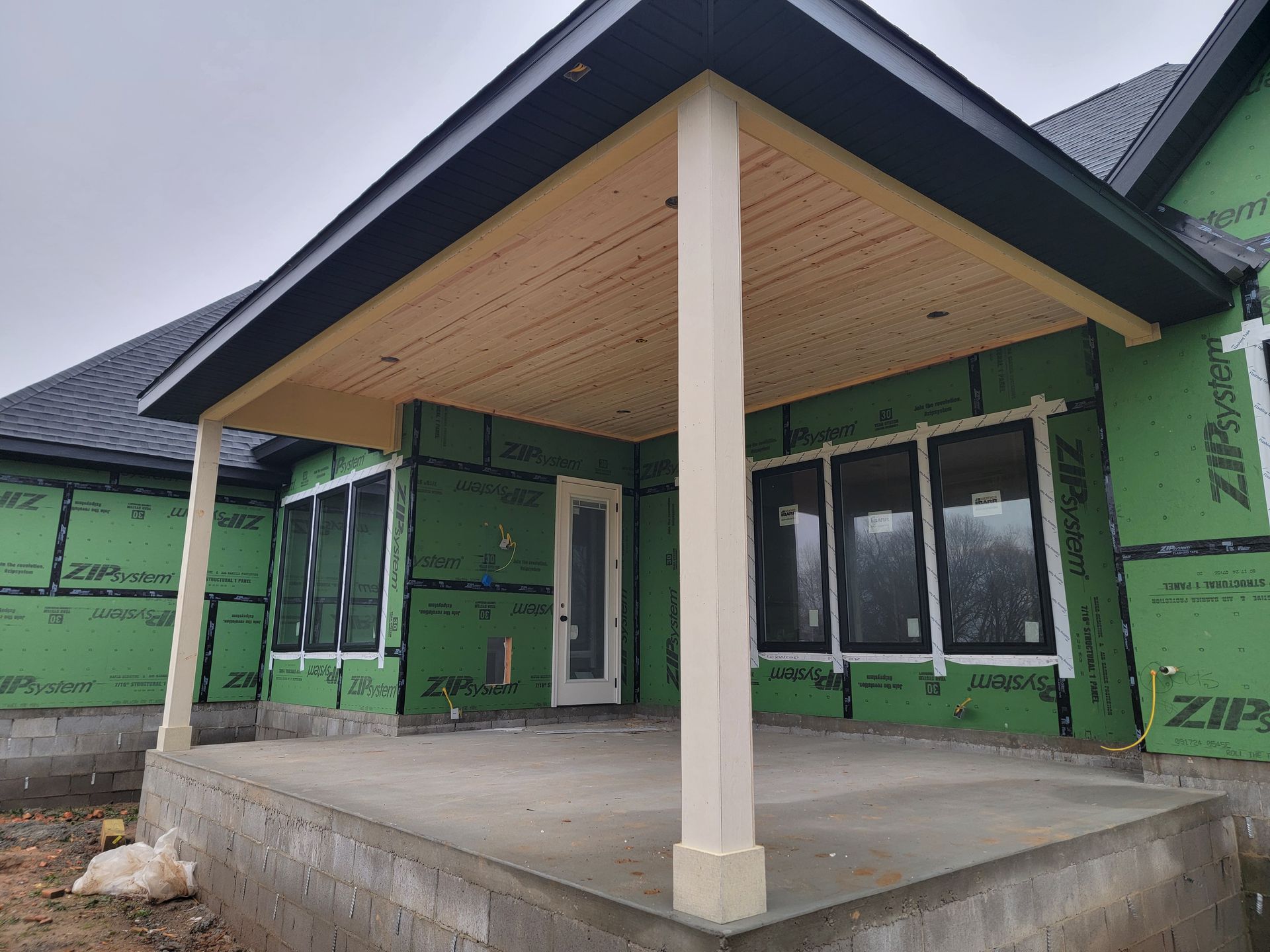 Partially built house porch with concrete slab, white columns, and green sheathing on the walls