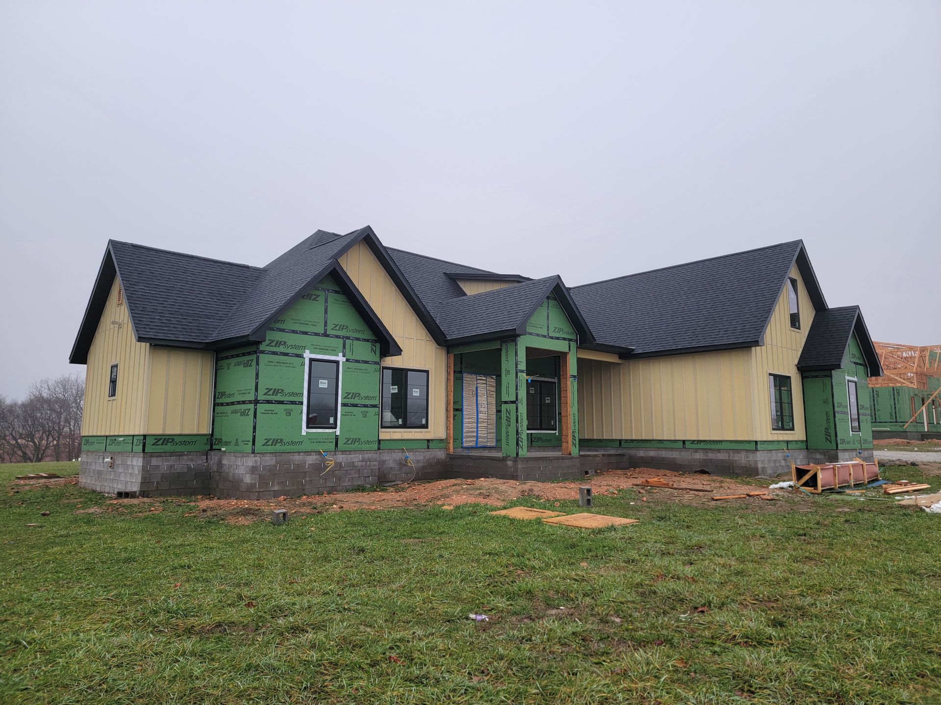 Partially built single-story house with yellow siding, green trim, and dark roof on a grassy lot