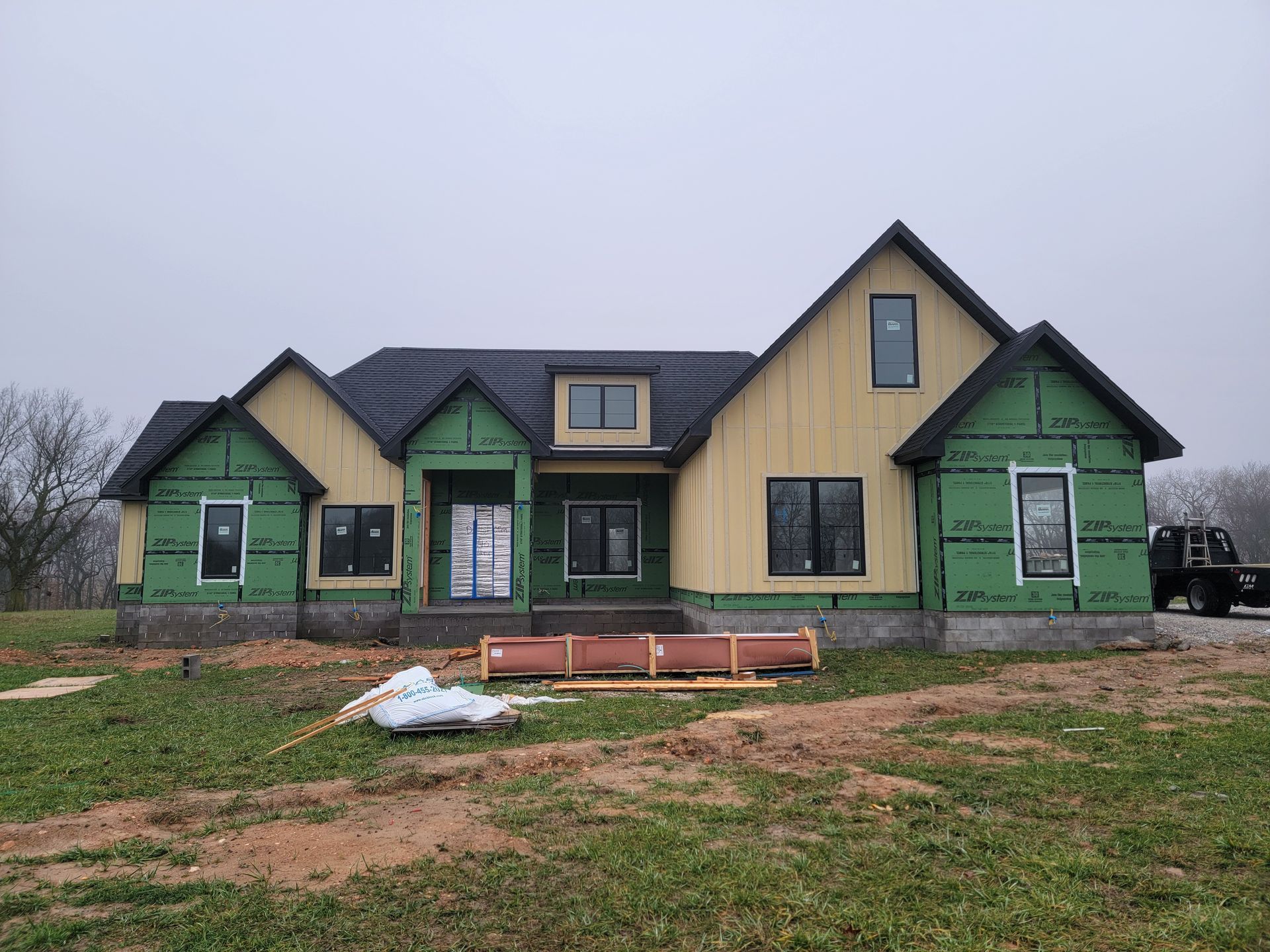Unfinished green house under construction with a dark roof and muddy yard in front