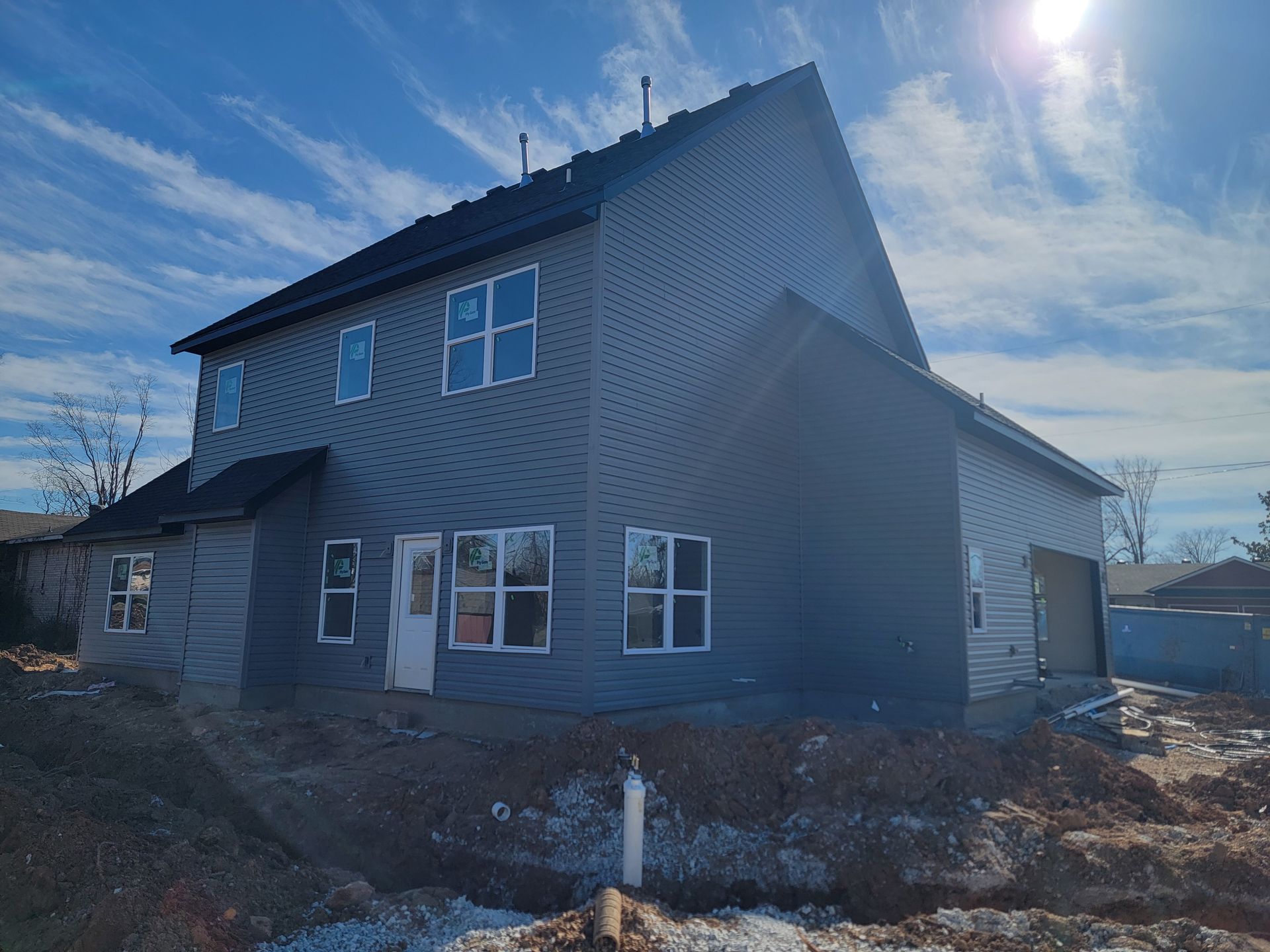 Two-story gray house under construction with unfinished yard and bright blue sky