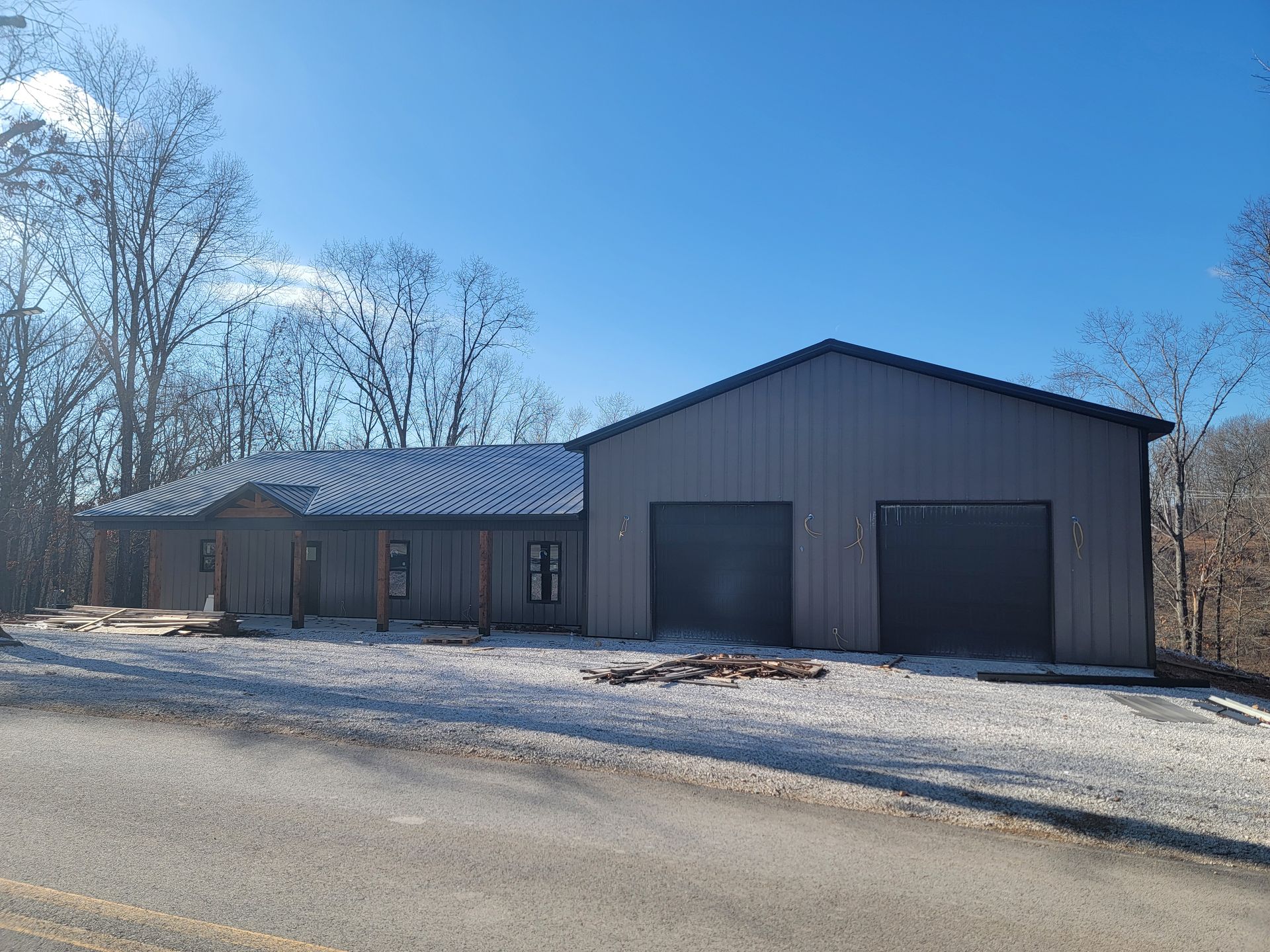 Snow-covered rural garage and house under a clear blue sky.