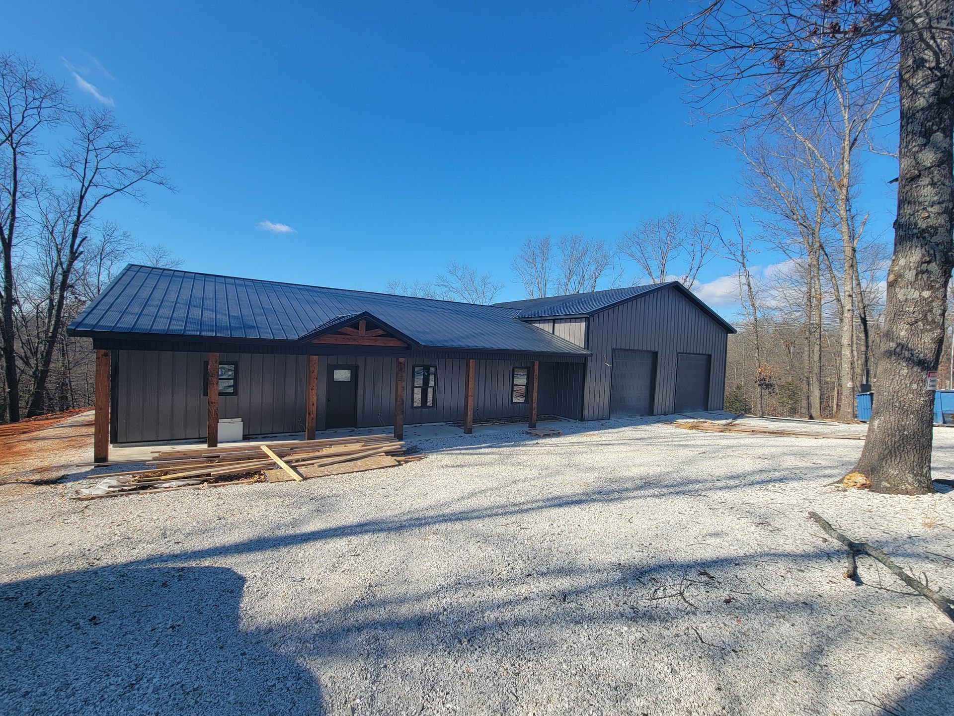 Rustic cabin with dark roof in a snowy yard, surrounded by leafless trees under a clear blue sky