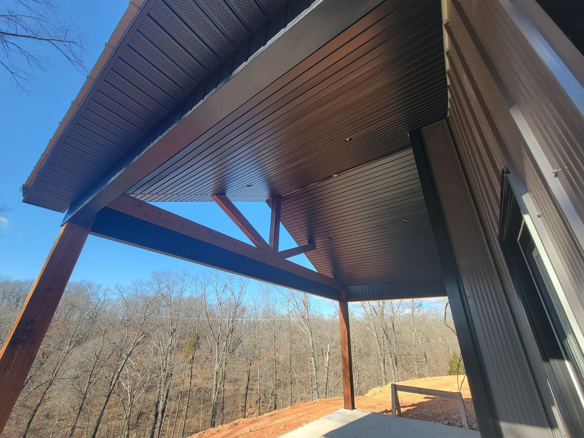 Covered outdoor patio with wooden ceiling and support beams overlooking trees and open landscape