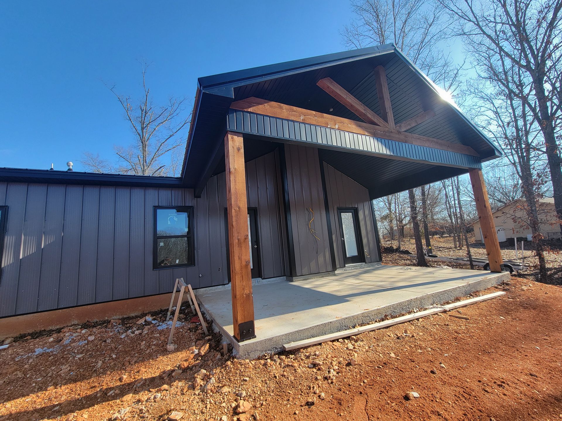 Small modern cabin with wood siding, covered porch, and tall timber posts on a sunny day