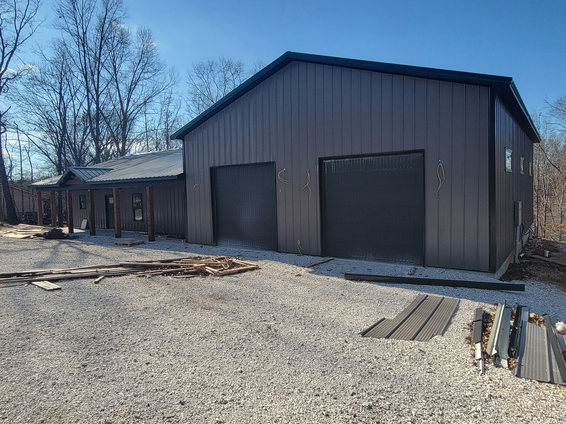 Large brown barn-style shed with garage doors on a gravel lot under a clear sky.