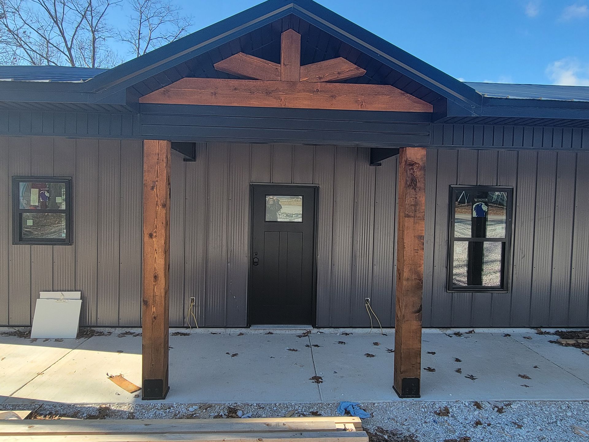 Front of a rustic cabin with a dark door, wooden posts, and snow on the ground.