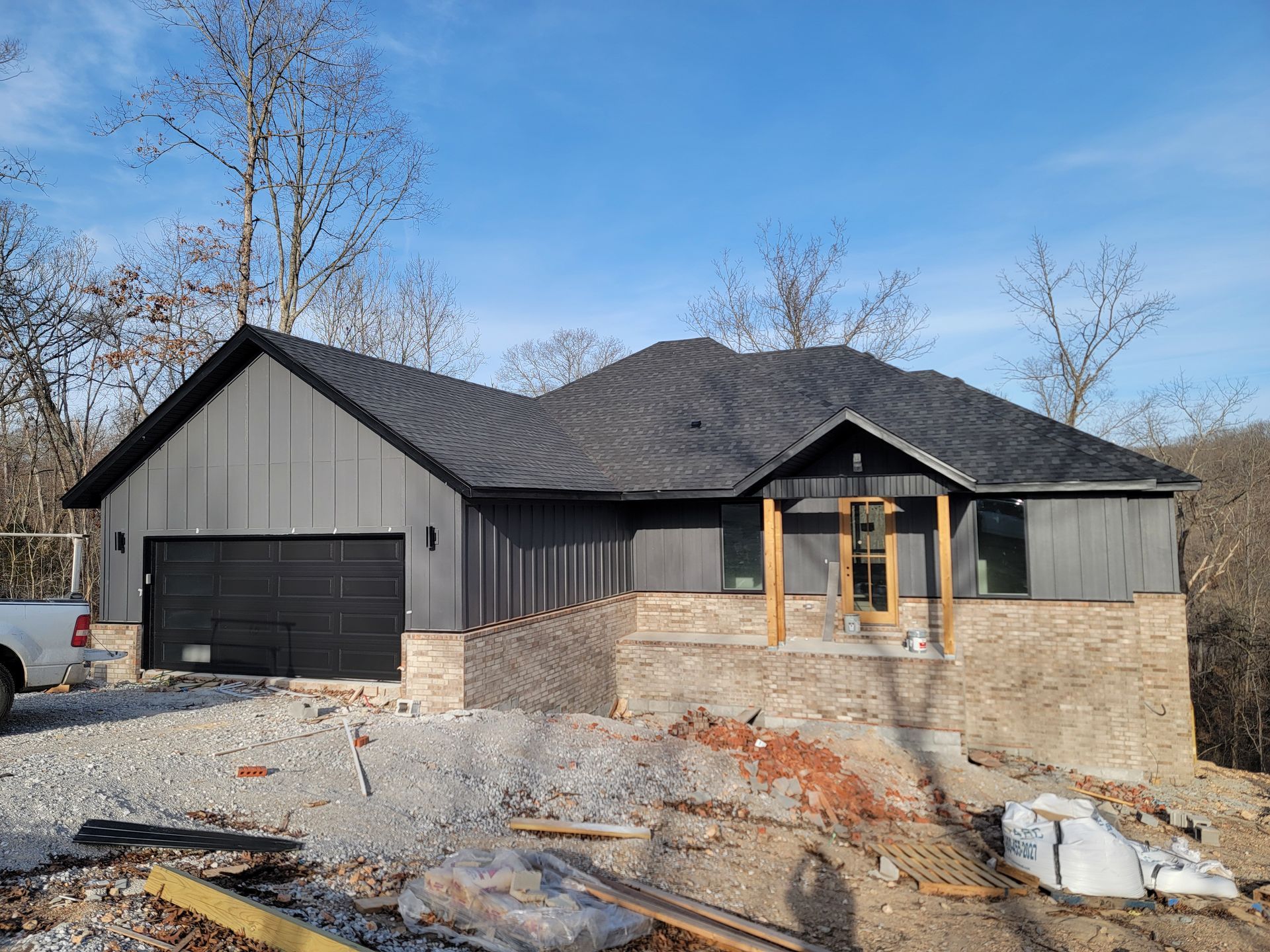 New gray house under construction with dark roof, unfinished brick porch, and gravel yard