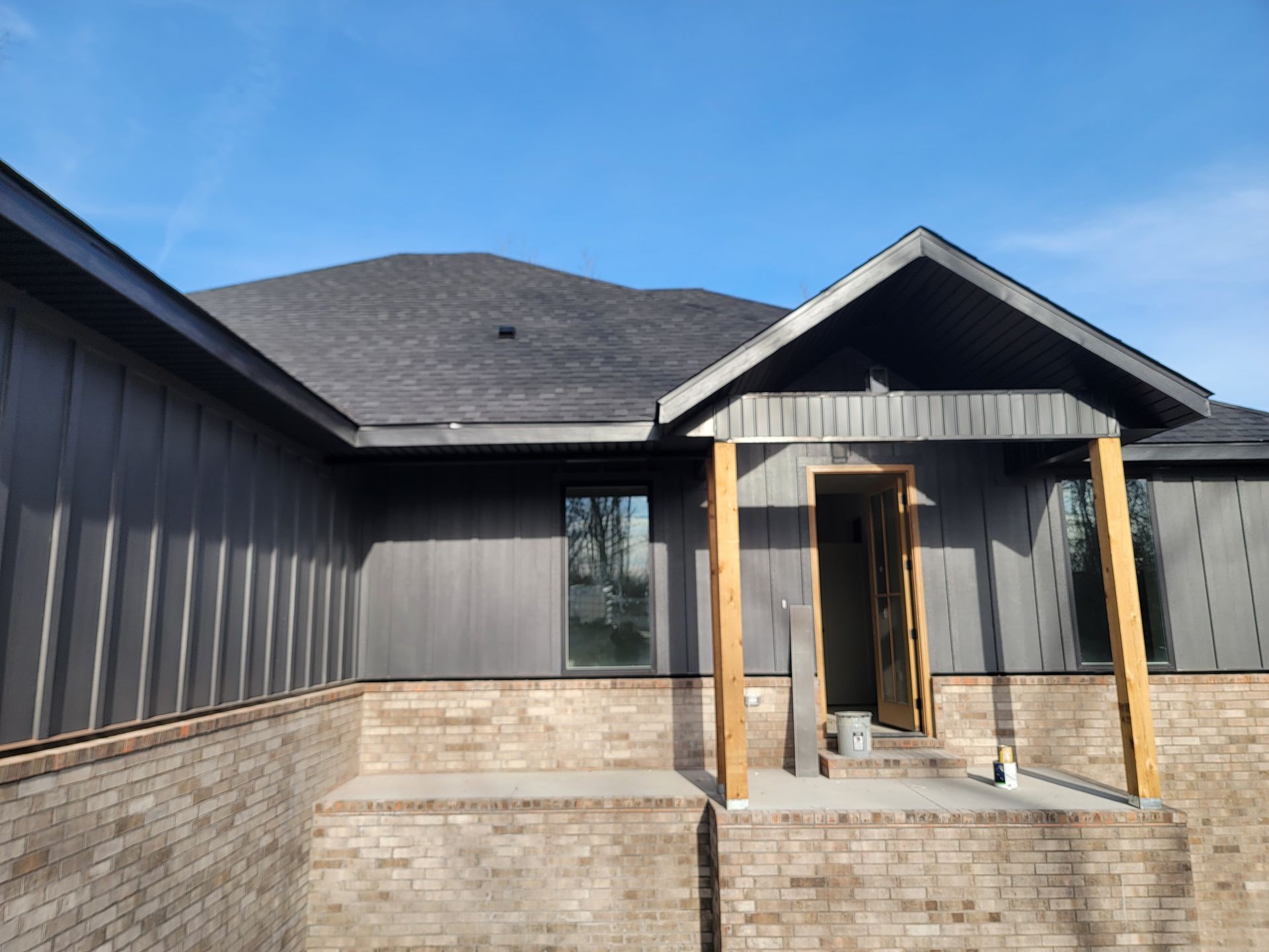 Front view of a gray house with a covered porch and stone base, under construction or unfinished.
