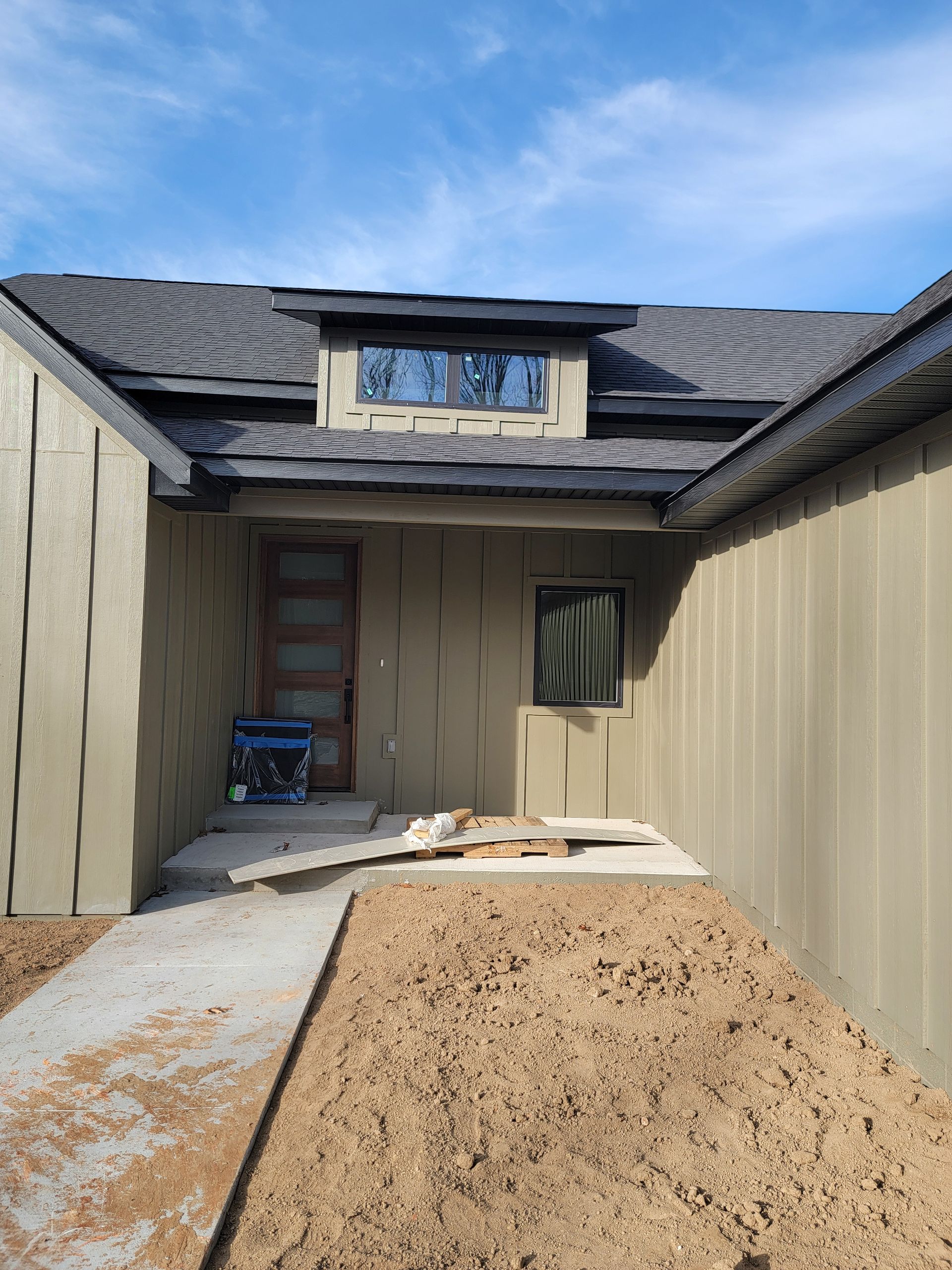 Narrow stucco courtyard with tan walls, shingled roof, and a doorway at the far end under blue sky