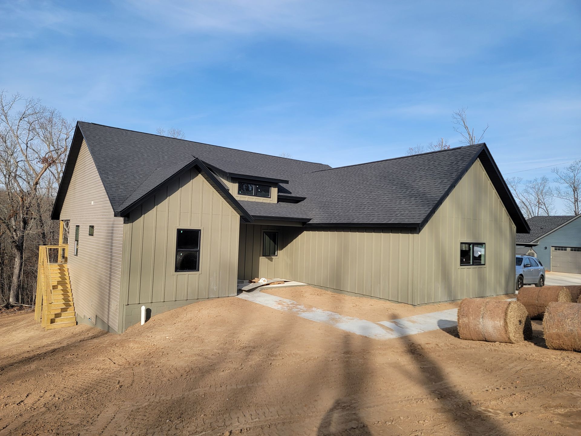 New house with dark roof and tan siding on a dirt lot under a clear sky