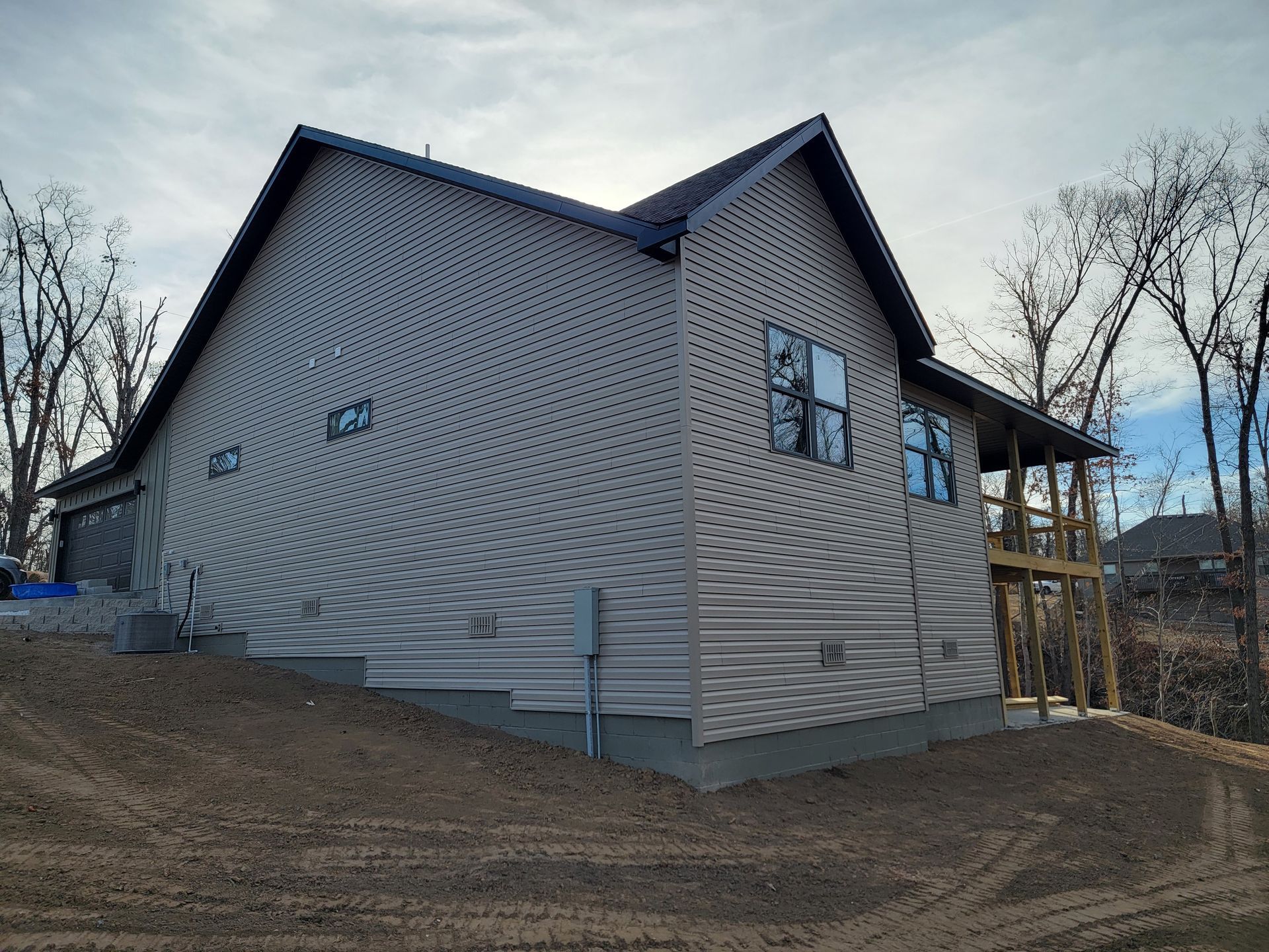Gray house on a sloped dirt lot with a wooden deck and leafless trees nearby