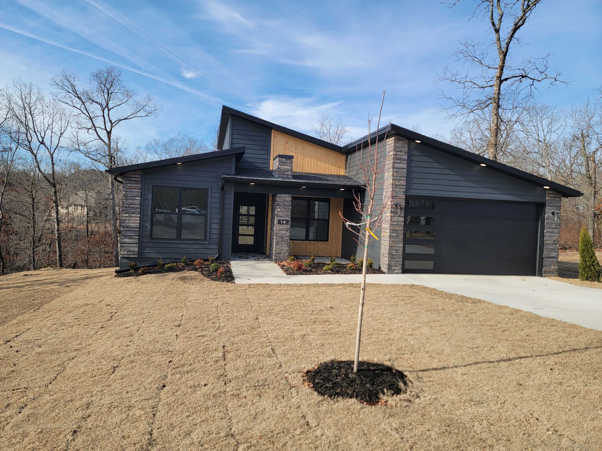 Modern single-story house with dark siding, stone accents, and a two-car garage in a winter yard.