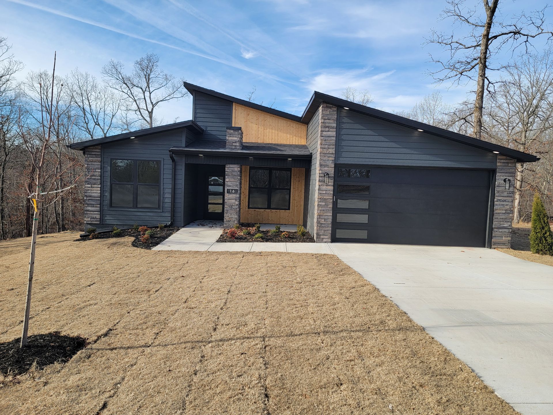 Modern dark-gray house with a two-car garage, concrete driveway, and sparse front yard.