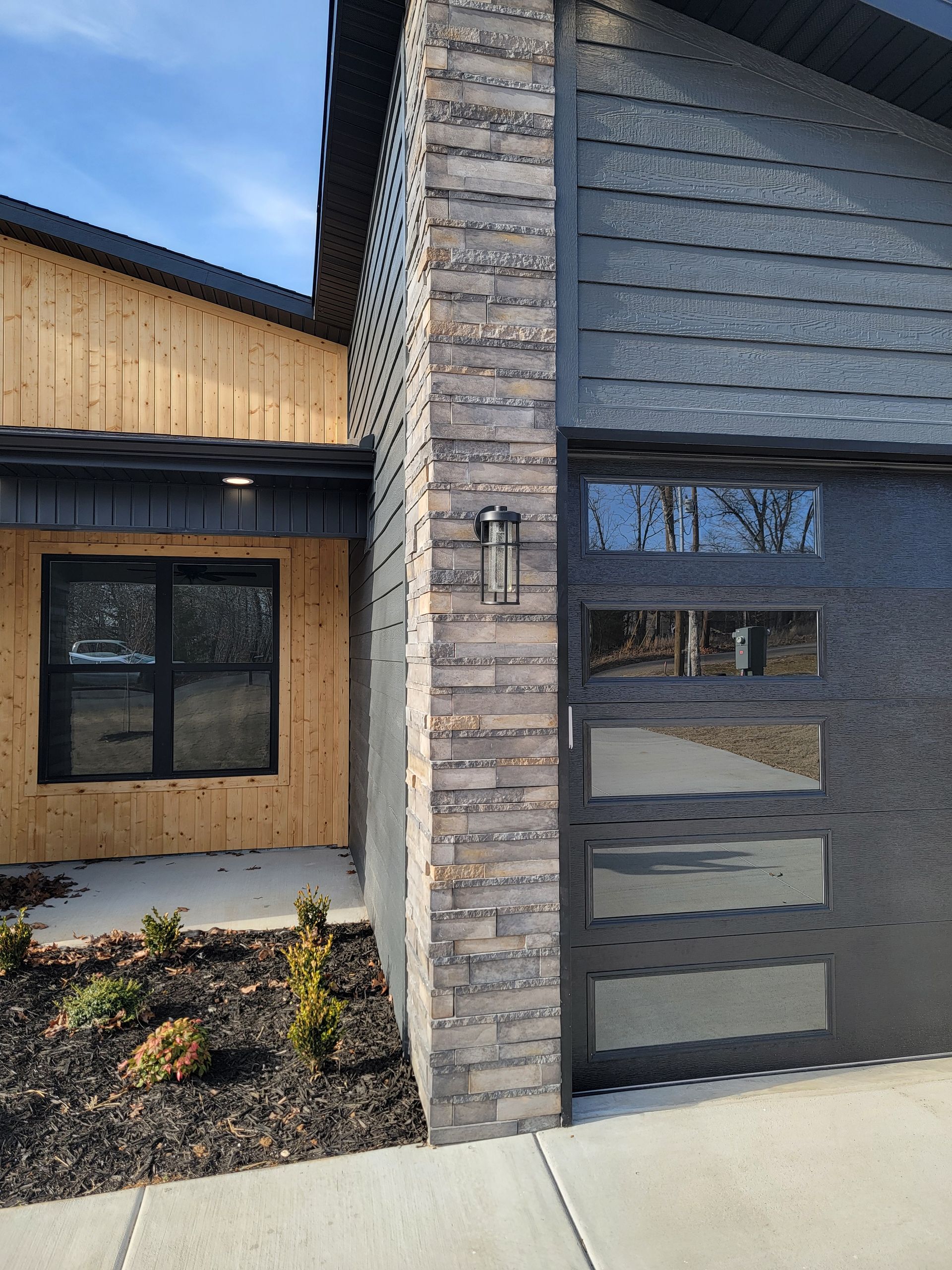 Modern house exterior with wood siding, brick column, and dark front door in daylight