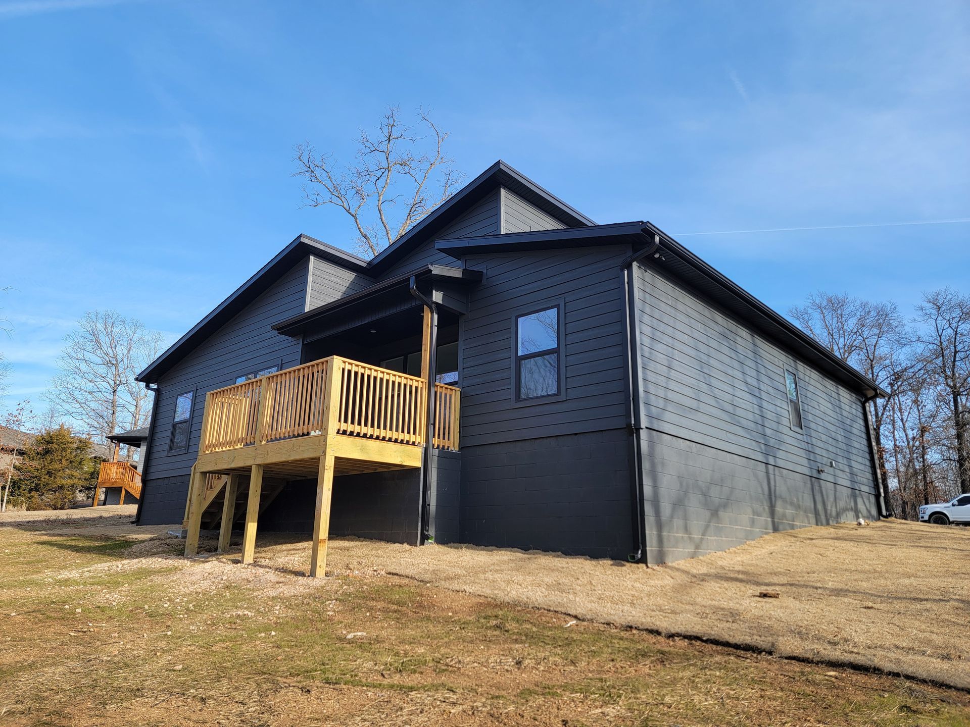 Black house with a wooden porch on a grassy hill under a clear blue sky