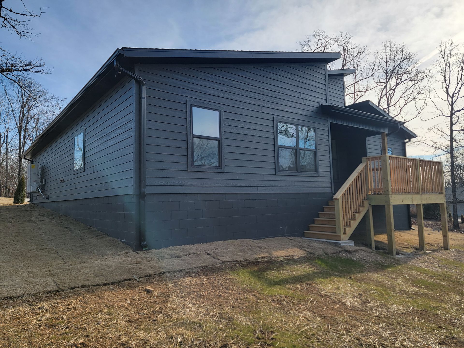 Gray house with a wooden front porch and stairs on a grassy lot under a clear sky