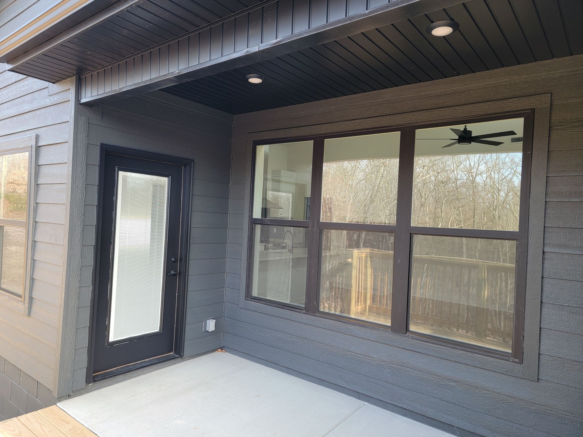 Covered porch with dark gray siding, a black door, and a large window overlooking a fenced yard