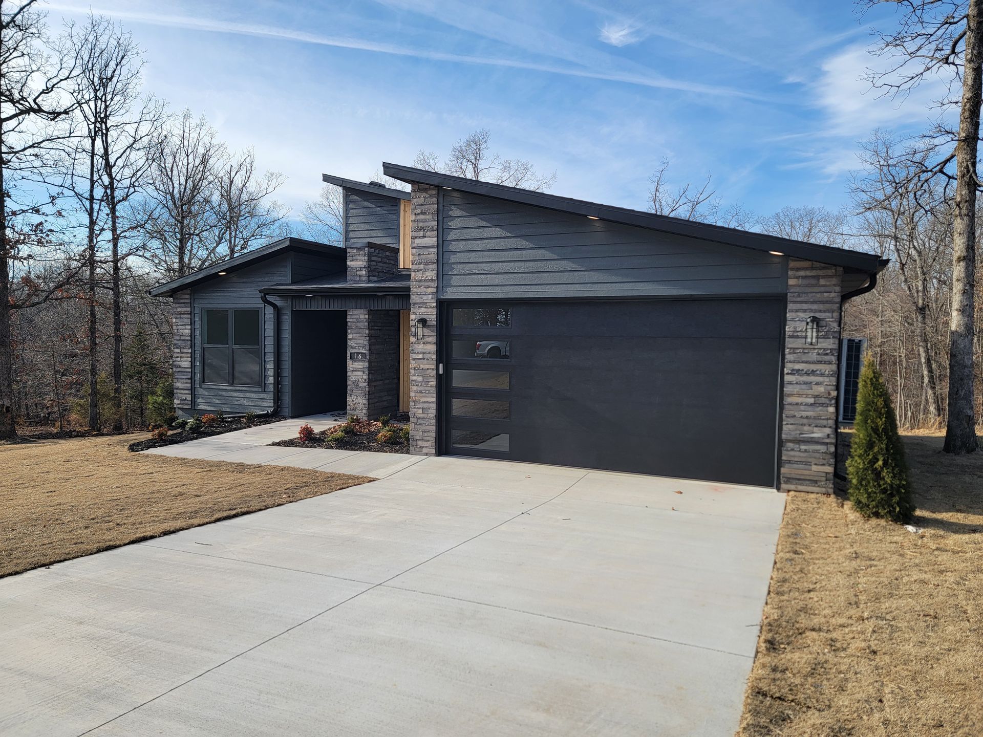 Modern gray single-story house with a large garage and concrete driveway under a blue sky