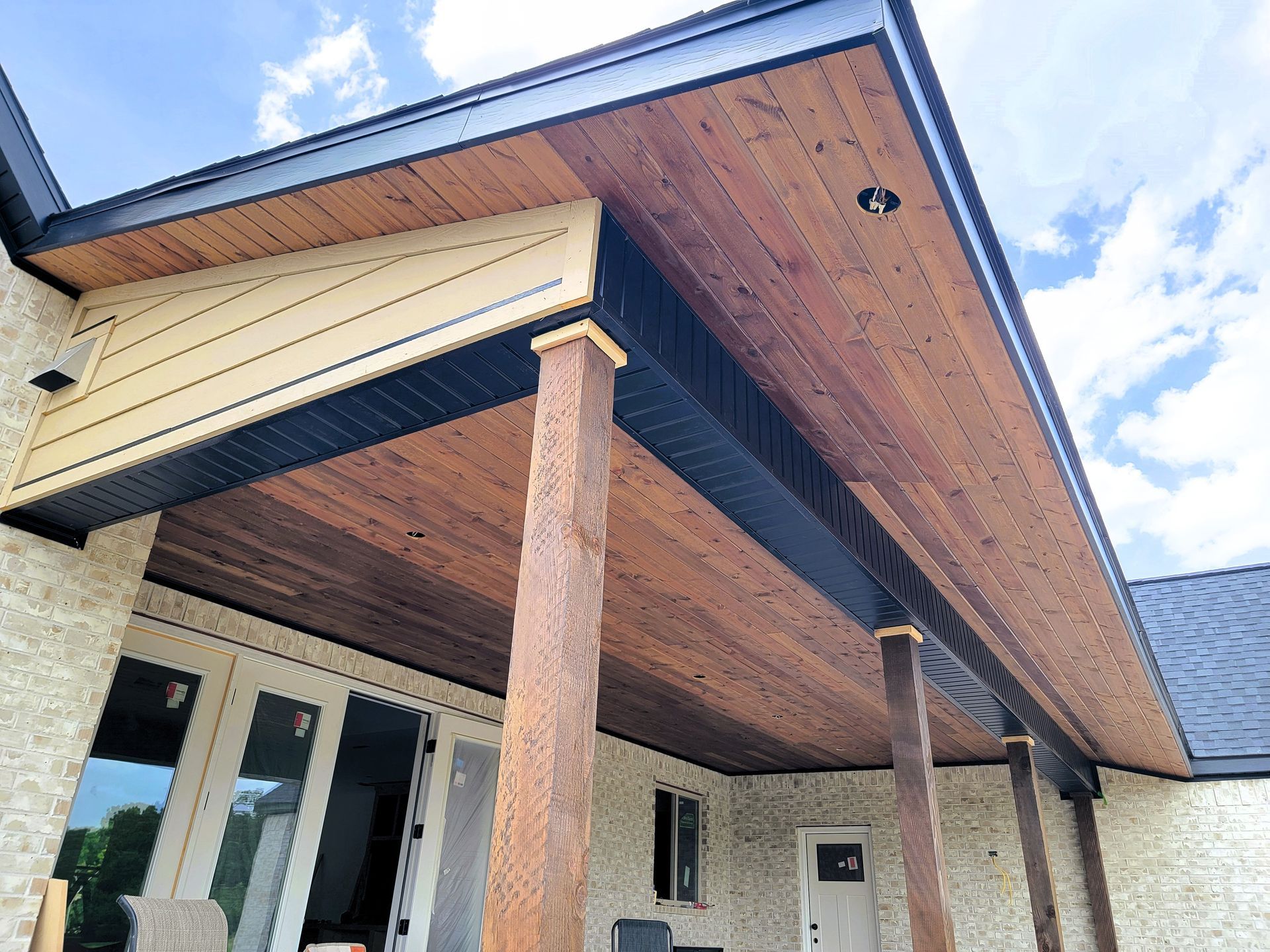 Covered porch with wood ceiling, two stone columns, and an exterior entrance under a blue sky