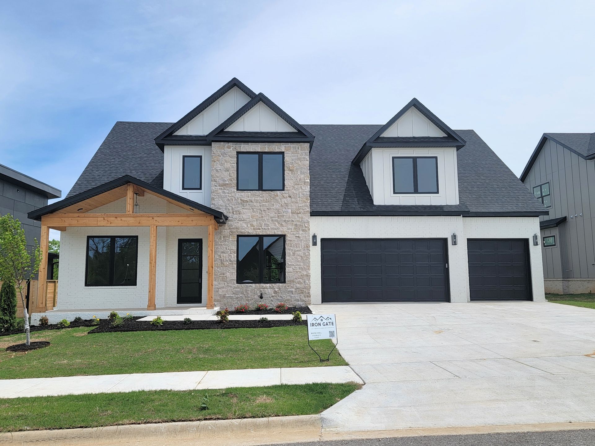 Modern two-story suburban house with black garage doors, light stone facade, and a wide driveway