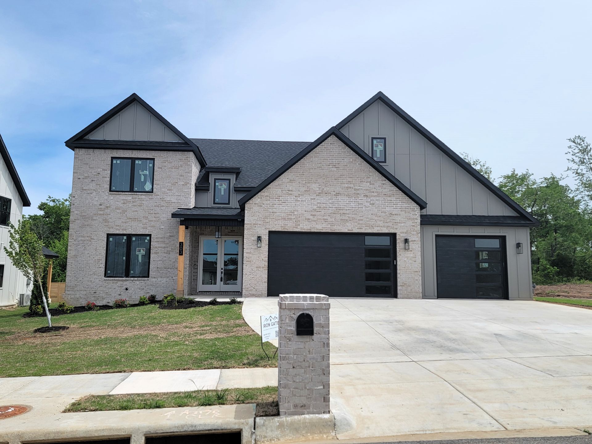 Modern two-story gray house with black garage doors, driveway, and brick mailbox under a clear sky