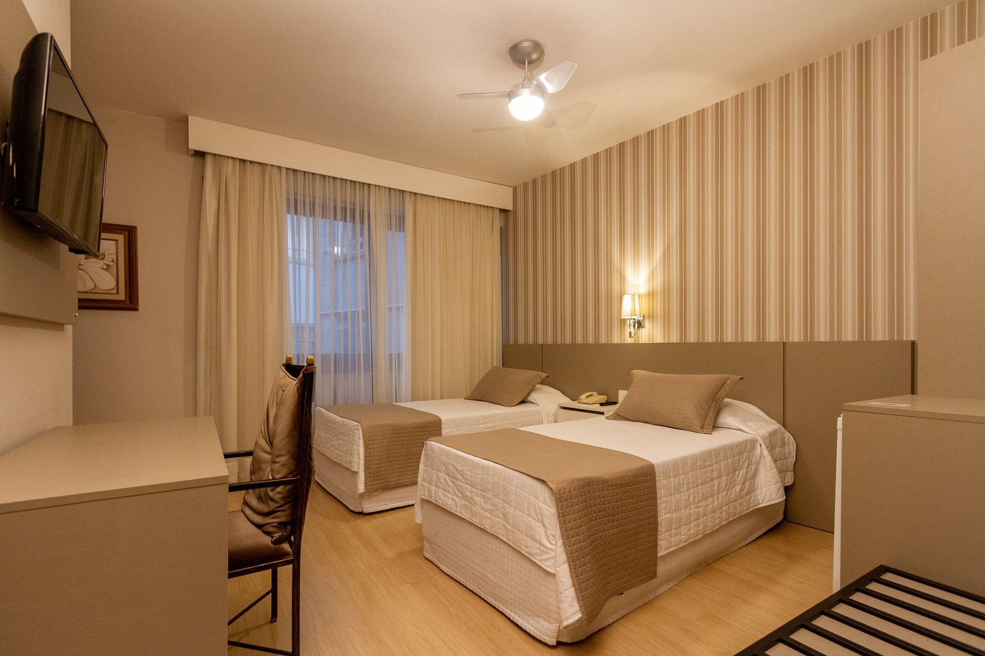 Um quarto de hotel com duas camas, uma escrivaninha e uma televisão.