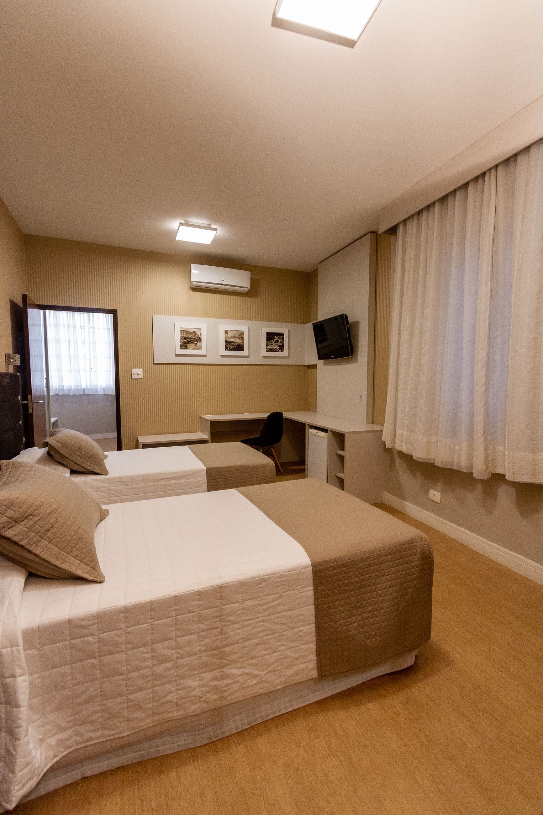 Um quarto de hotel com duas camas, uma escrivaninha e uma televisão.