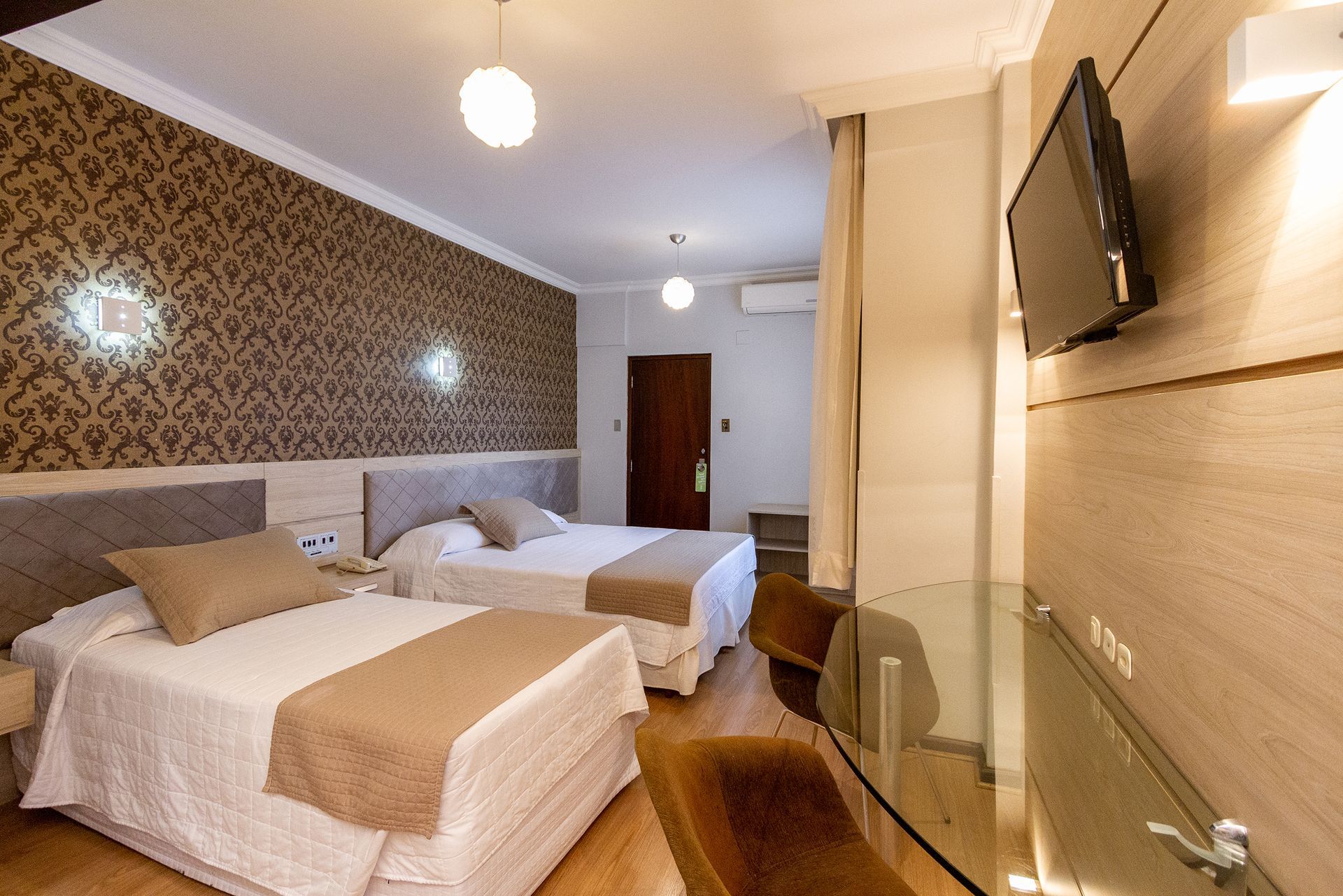 Um quarto de hotel com duas camas, uma escrivaninha e uma televisão.