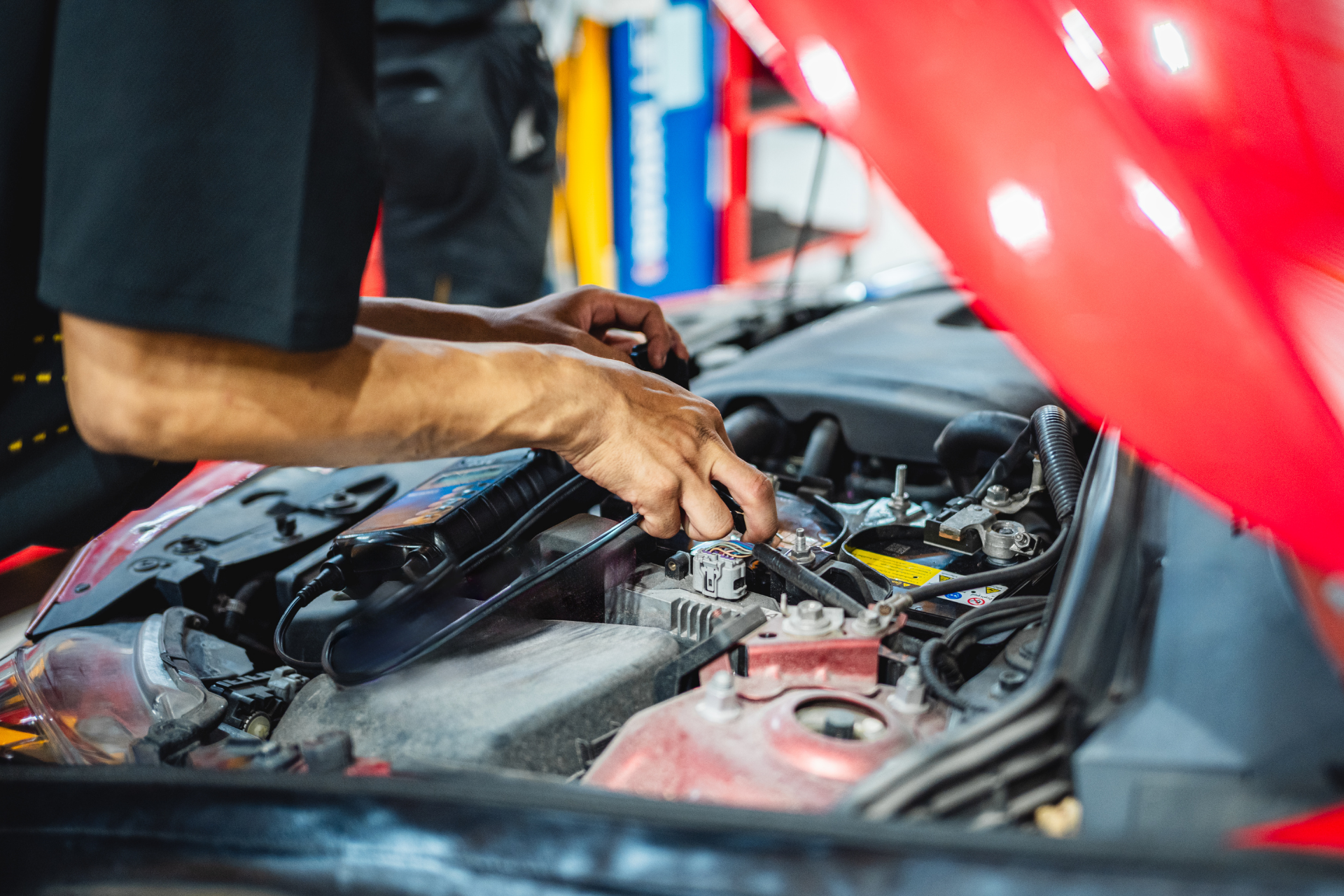 Mechanic working on a car engine with the hood open.