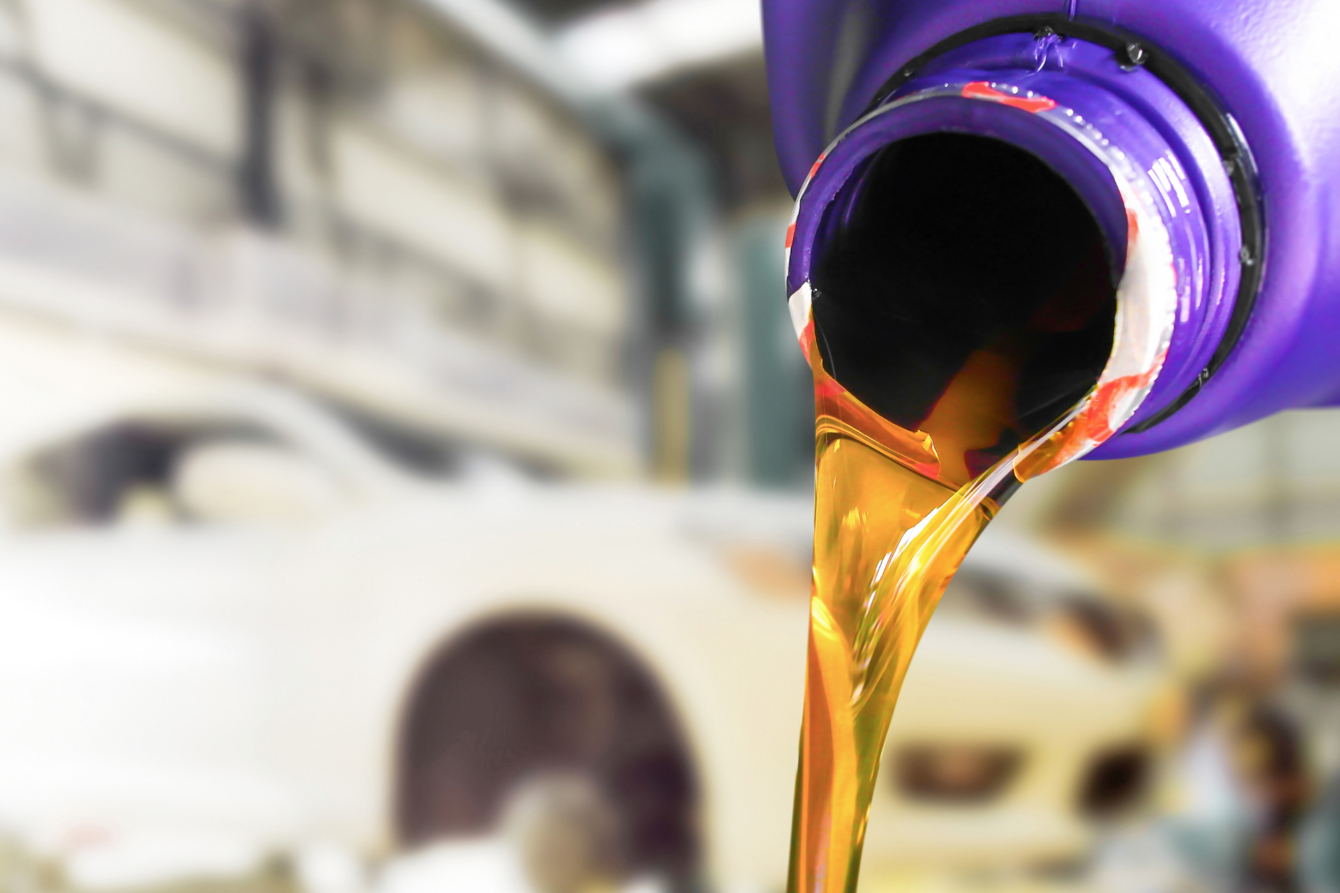 Oil pouring from a purple container into a car engine, in a mechanic's garage setting.