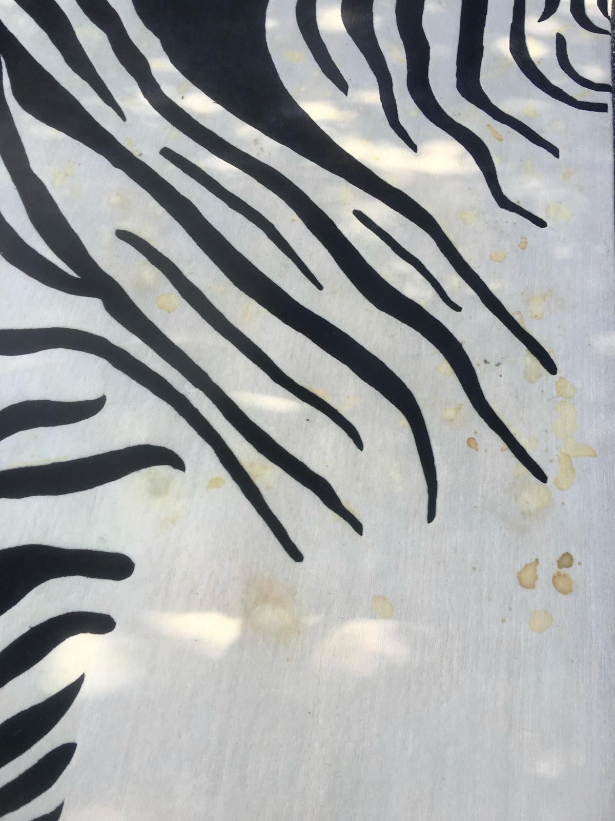 Zebra-striped rug with black stripes on a white background, stained with yellow spots.
