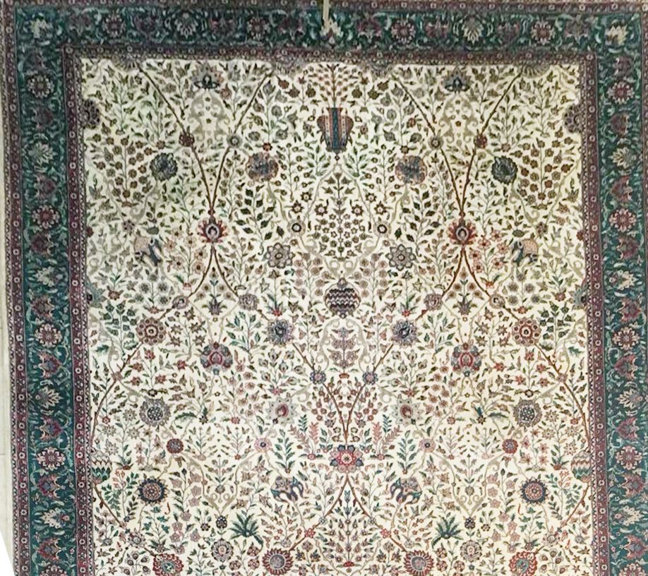 Cream-colored rug with floral patterns, green border, intricate design.