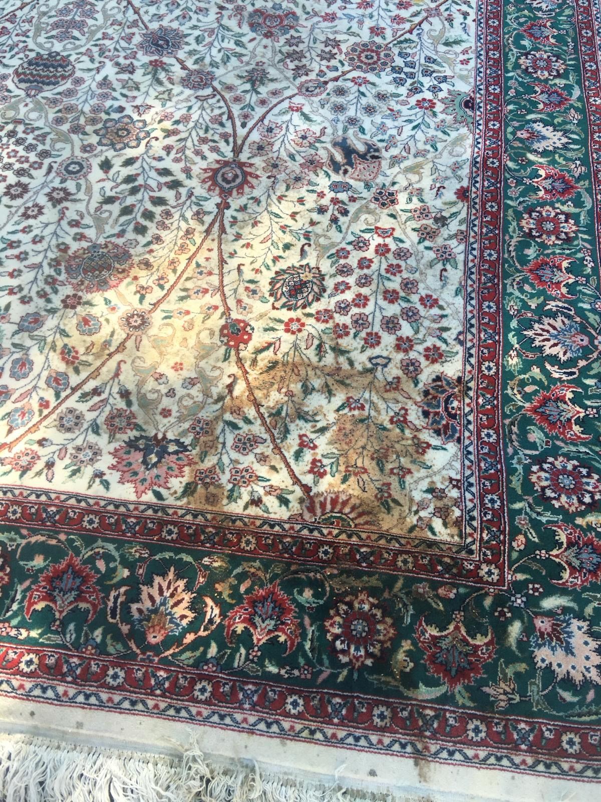 Cream-colored rug with brown stains, floral design, green and red border, and fringe.