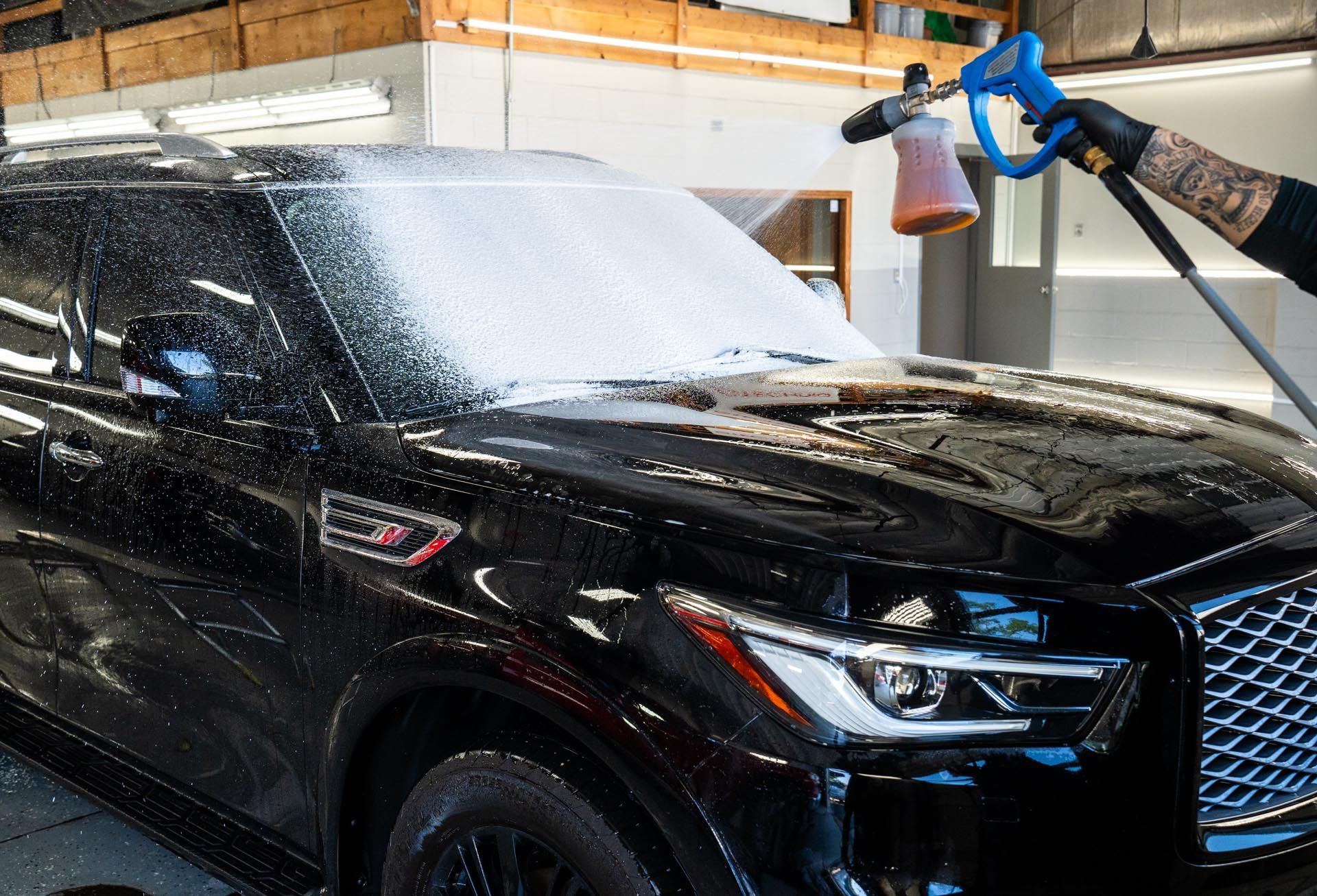 Black SUV being washed with foam, worker holding a foam cannon.