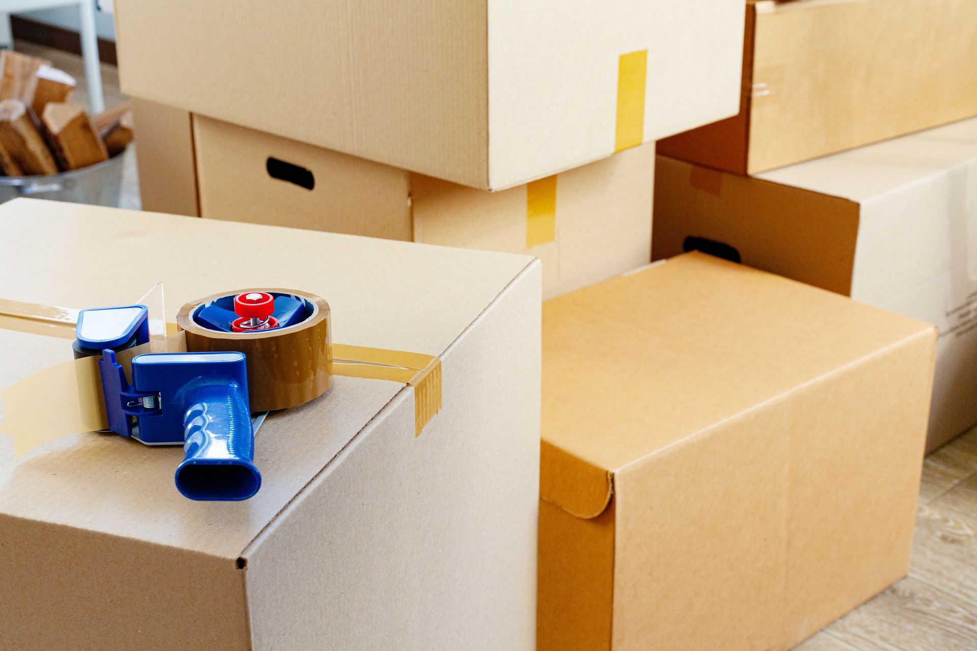 Stacked cardboard moving boxes with packing tape and a roll of tape on top in a storage area