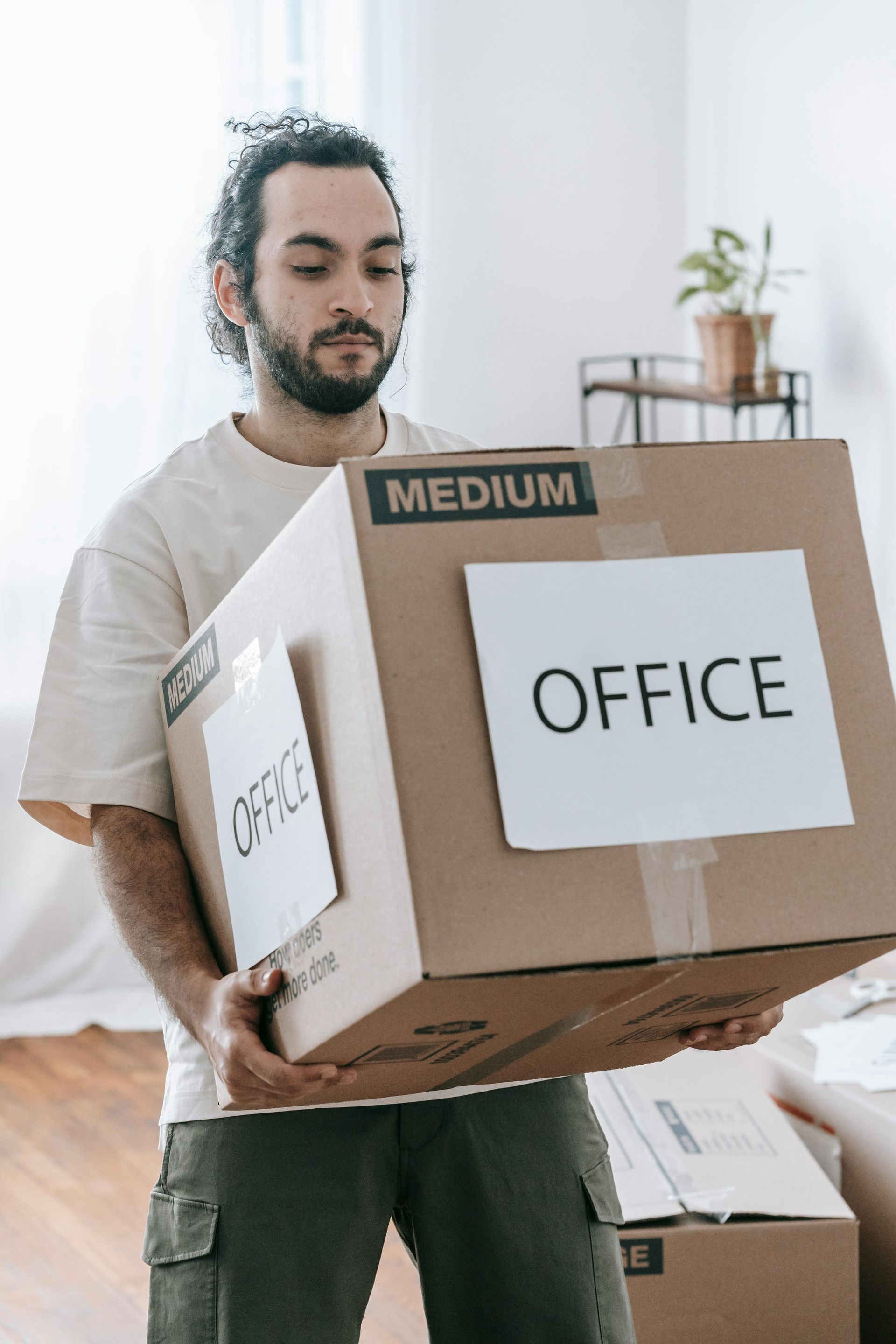Person carrying cardboard boxes labeled “OFFICE” in a bright room