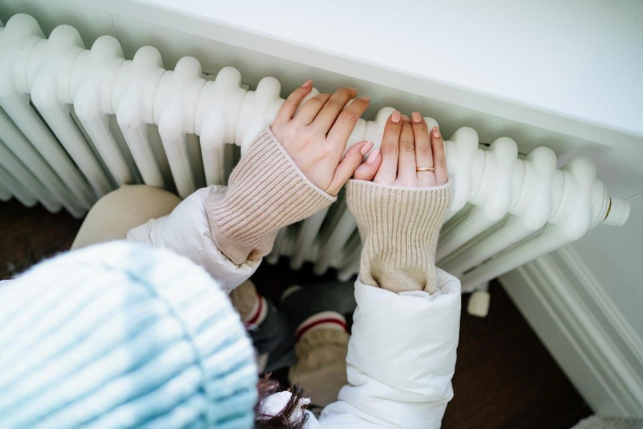 Una persona si scalda le mani su un termosifone.