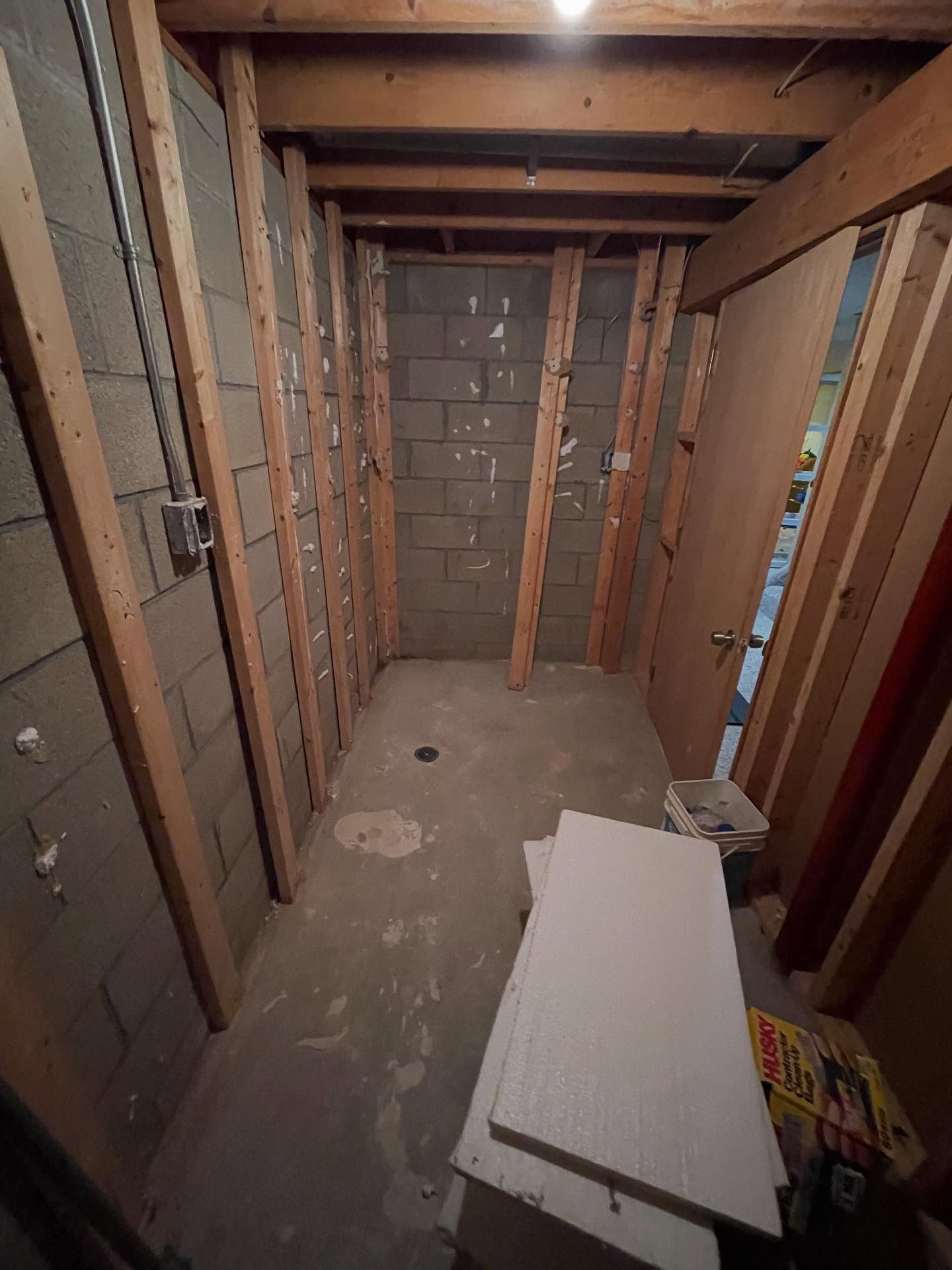 Unfinished basement with exposed studs, concrete walls, and construction materials on the floor.