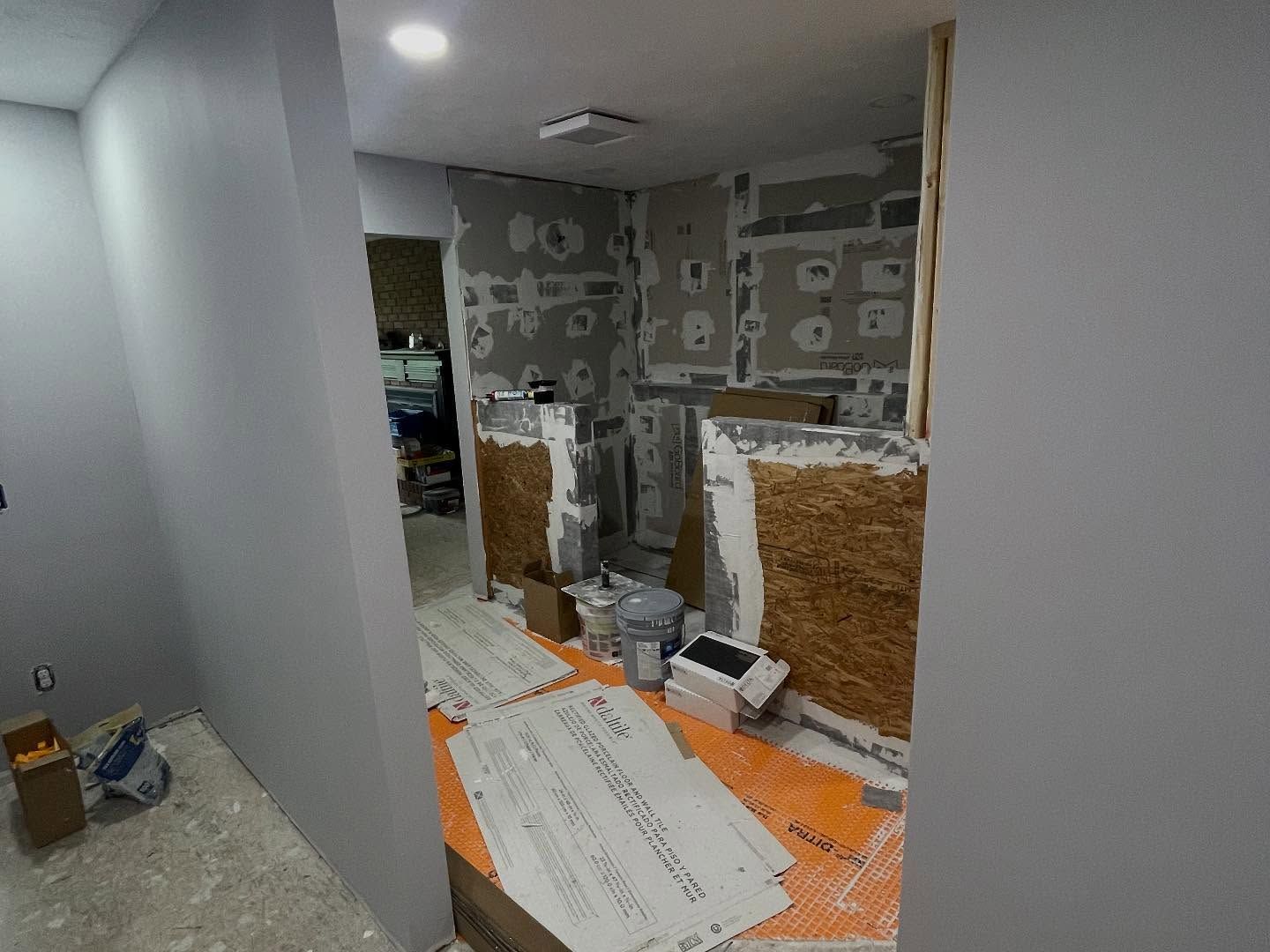 Partially renovated room with exposed walls, orange floor covering, and construction materials scattered around.