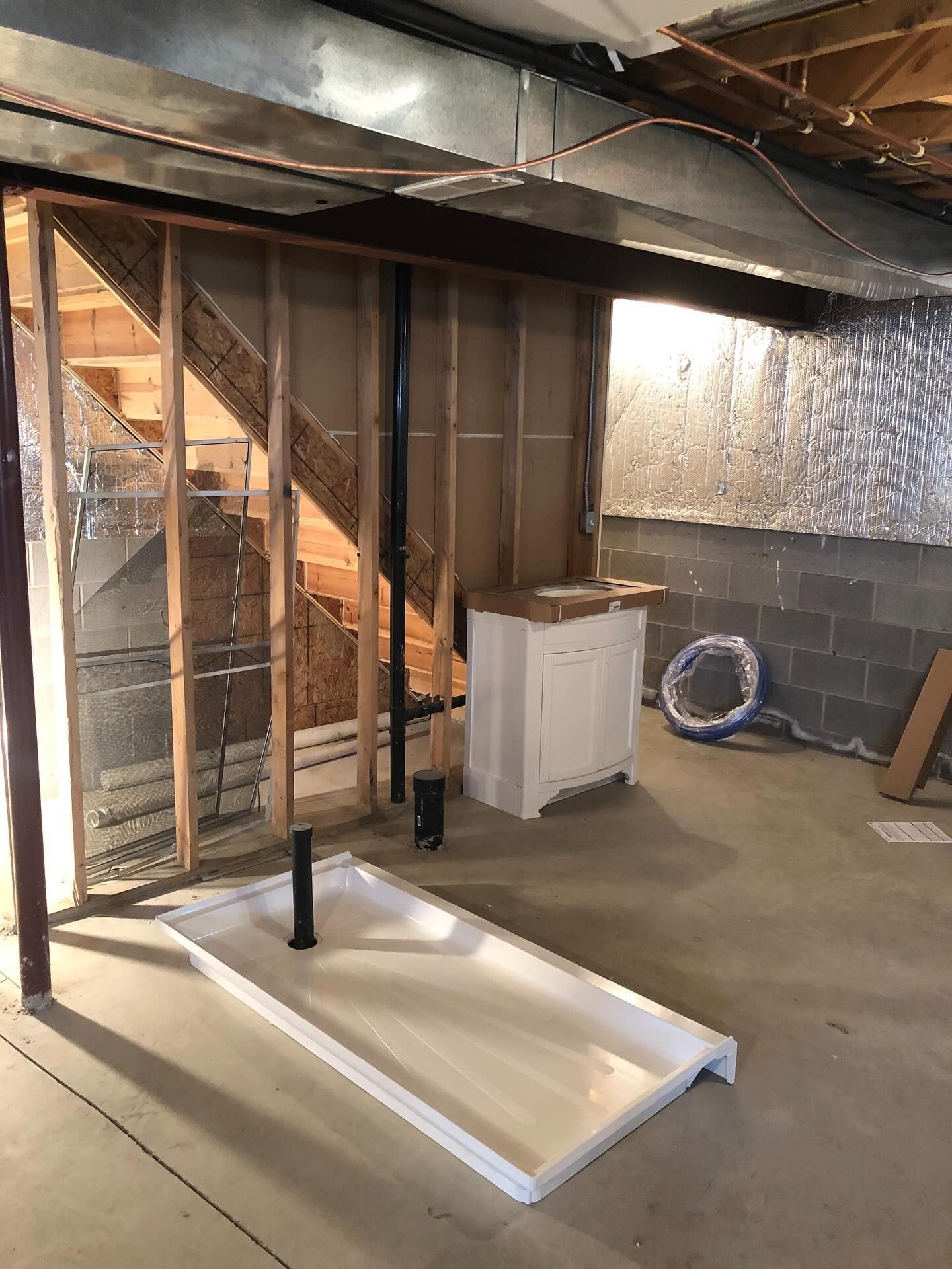 Unfinished basement with exposed framing, ductwork, furnace, and a dropped ceiling panel on the floor.